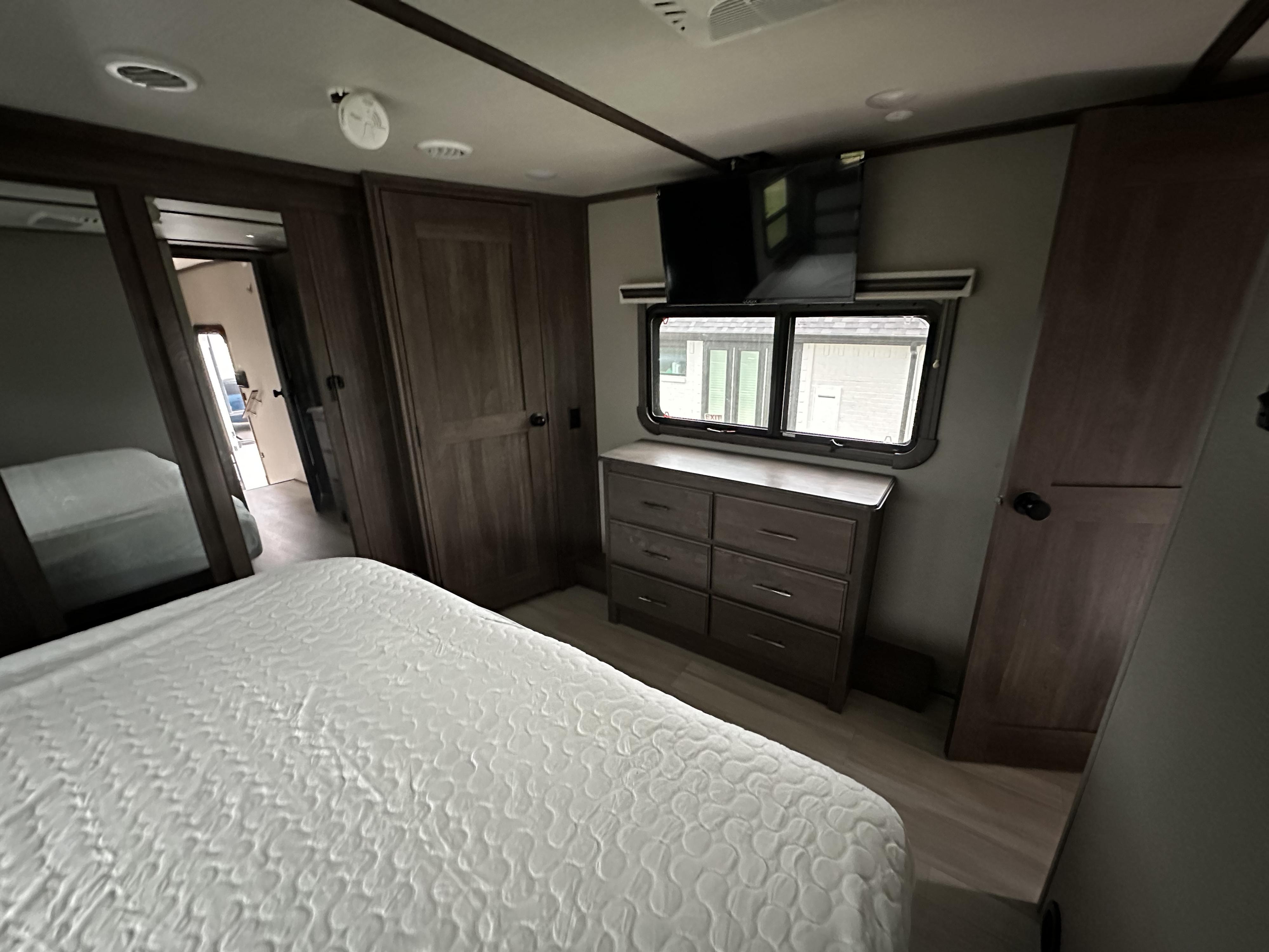 Inside an RV rental: a compact bedroom featuring a white bed, dresser, TV, and reflective closet door.. Grand Design Solitude 2022