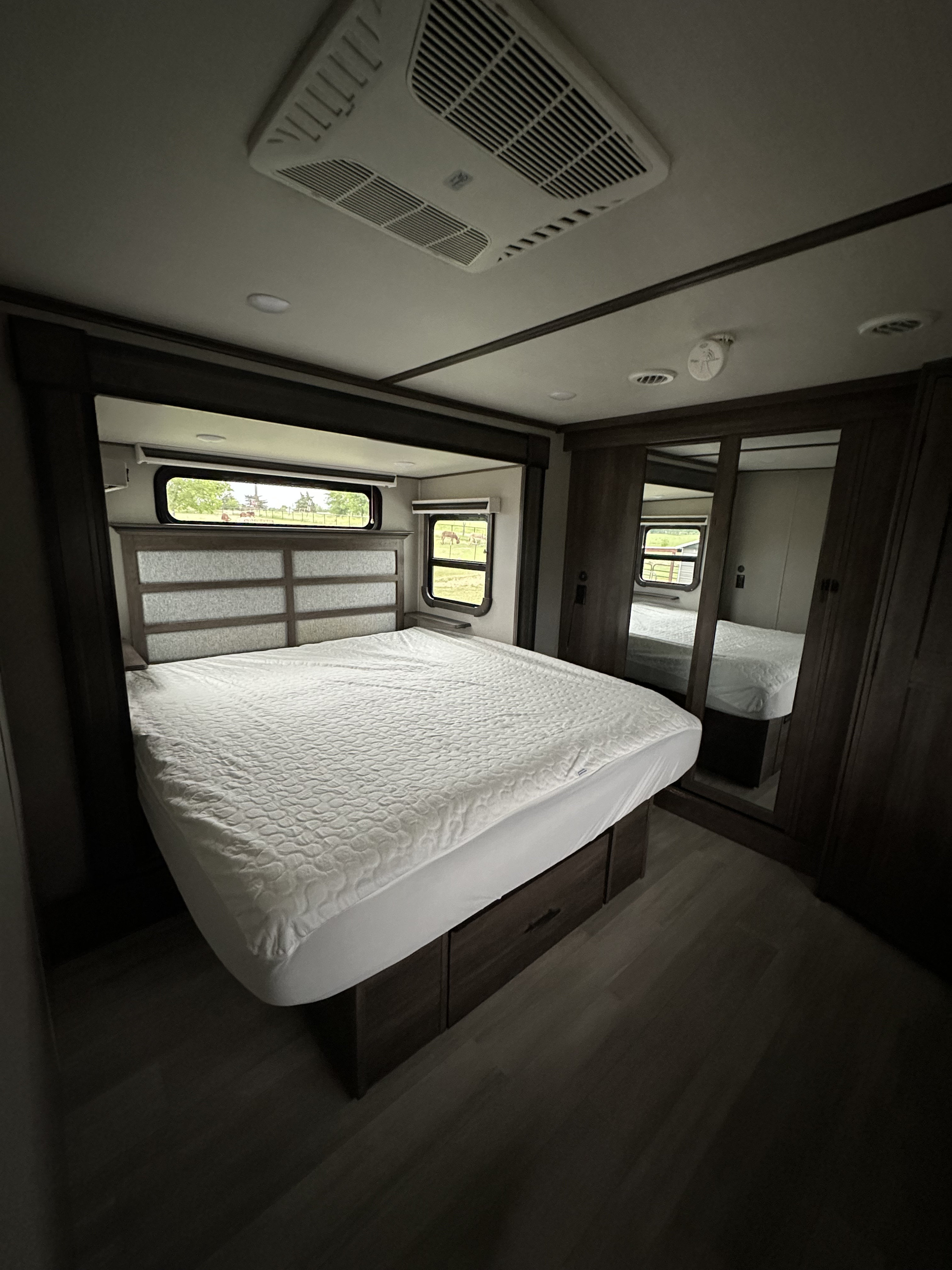 Spacious RV rental bedroom featuring a comfy bed, mirrored wardrobe, and scenic outdoor views from the windows.. Grand Design Solitude 2022