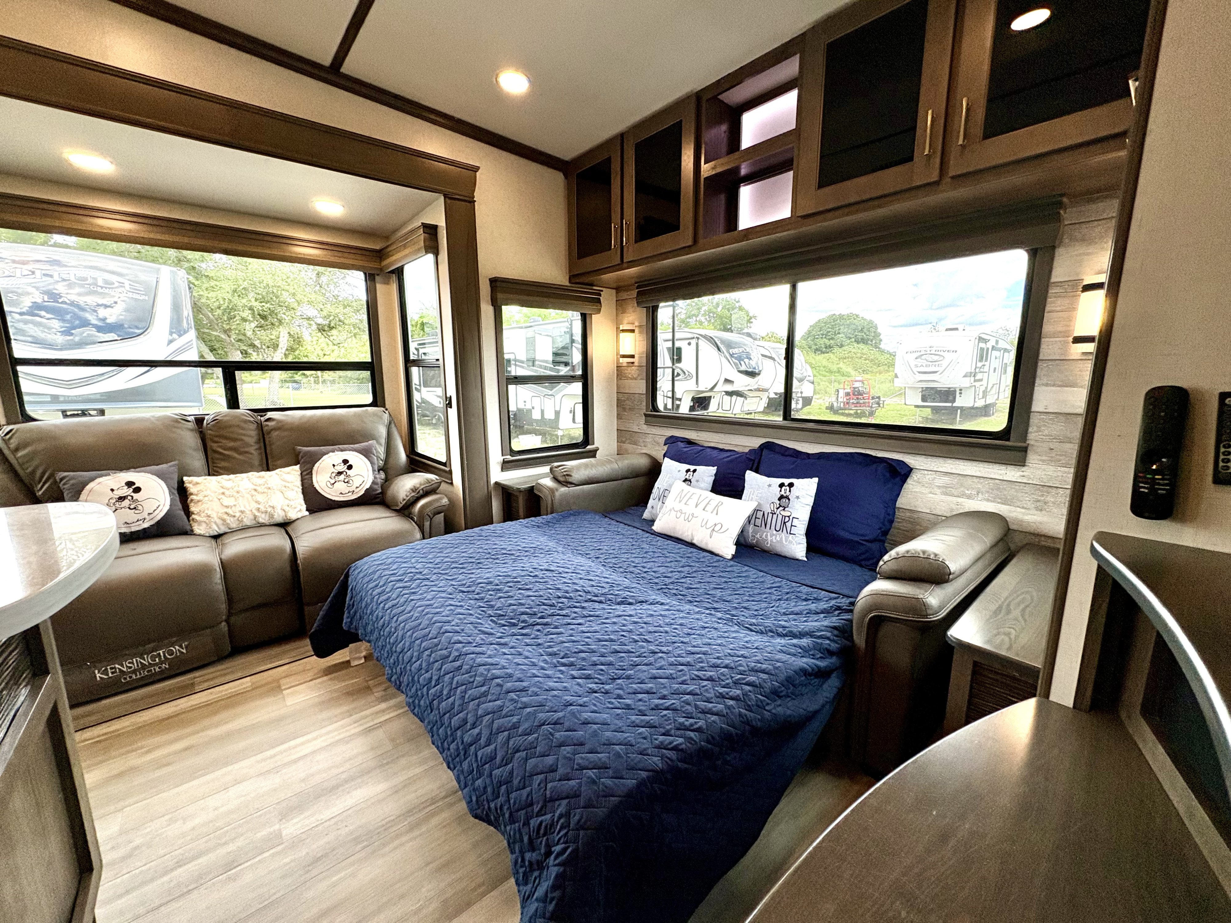 RV rental interior featuring a cozy bed with a blue quilt, a sofa, ample storage, and large windows with outdoor views.. Alliance Paradigm 2021