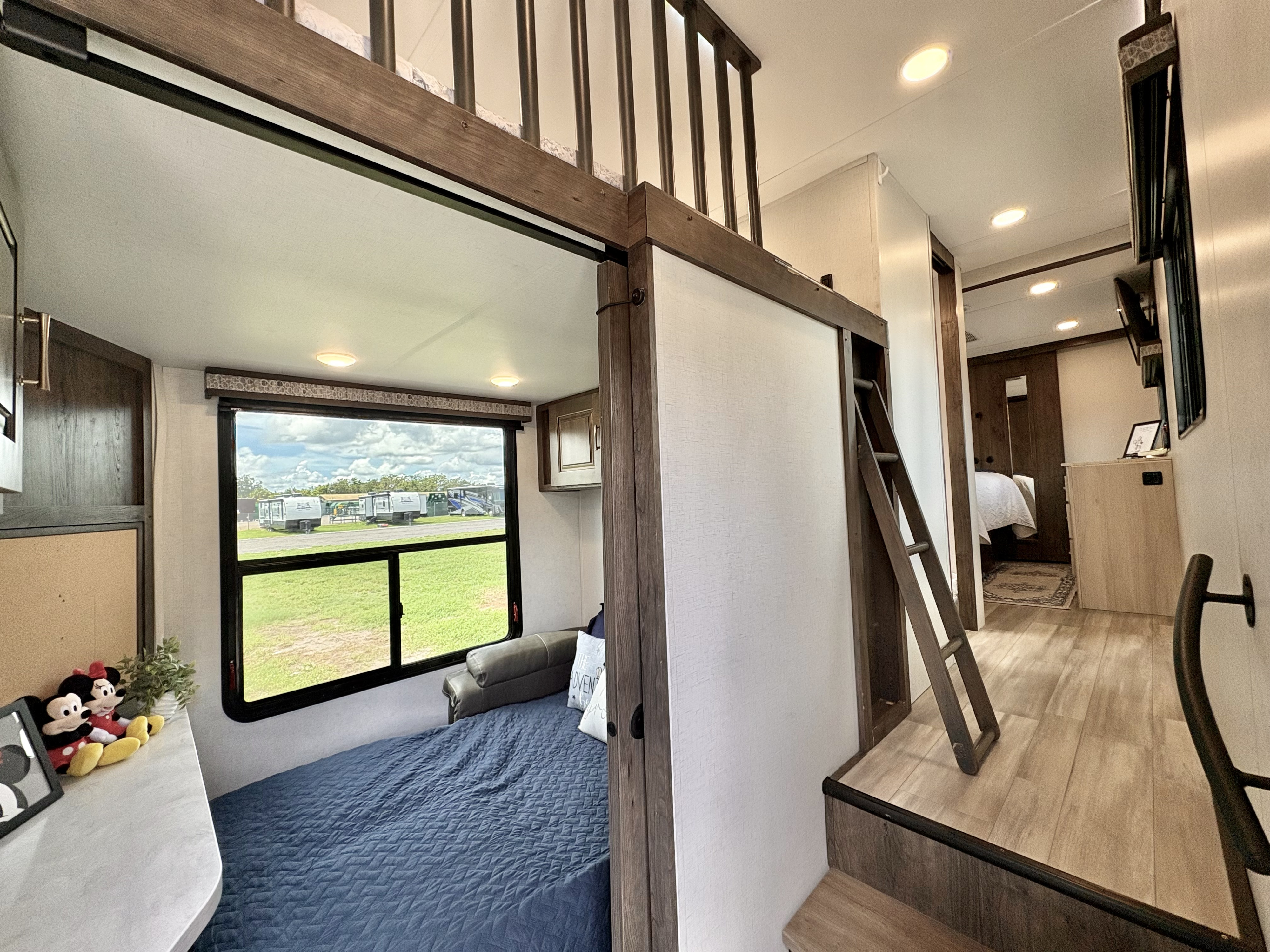 Modern RV rental interior: cozy loft with ladder, lower bed by a large window, and light wood accents.. Alliance Paradigm 2021