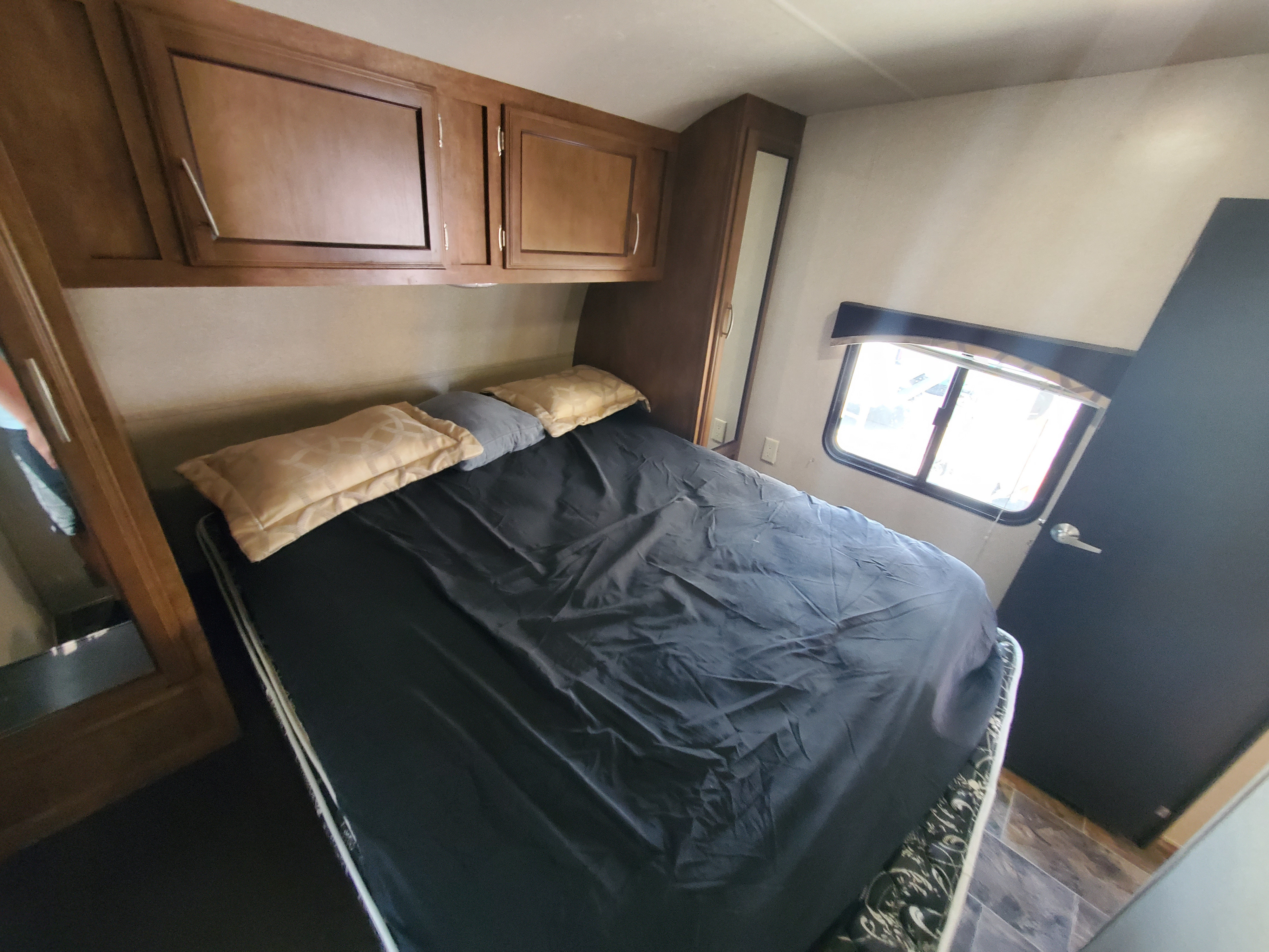 Cozy RV rental bedroom with a comfortable bed, overhead cabinets, a window, and ample storage space.. Forest River shockwave 2018