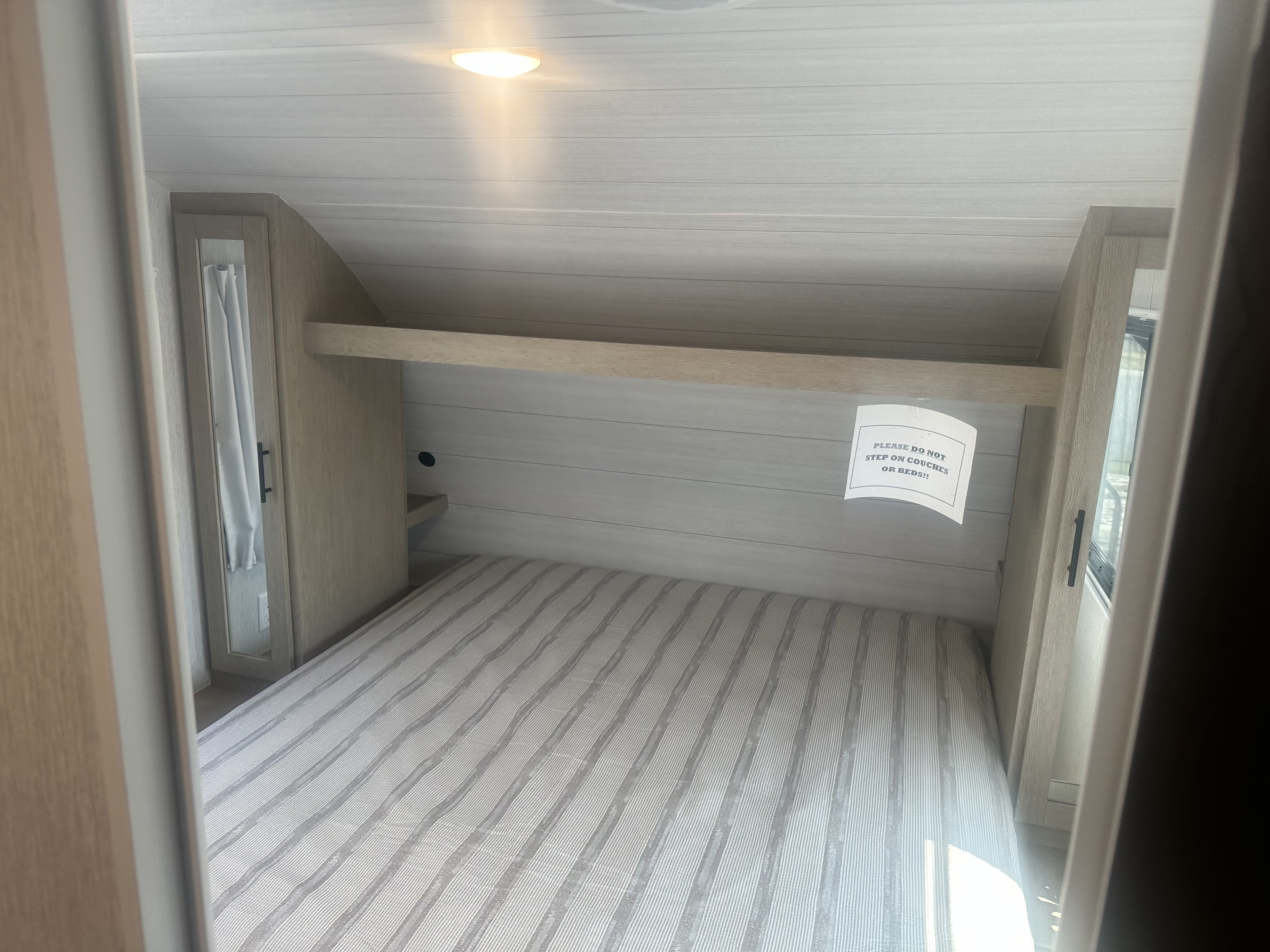 Bright RV rental bedroom showcasing a striped bed, built-in storage, and ceiling light. A sign prohibits stepping on beds.. Forest River Evo 2400bhl 2024