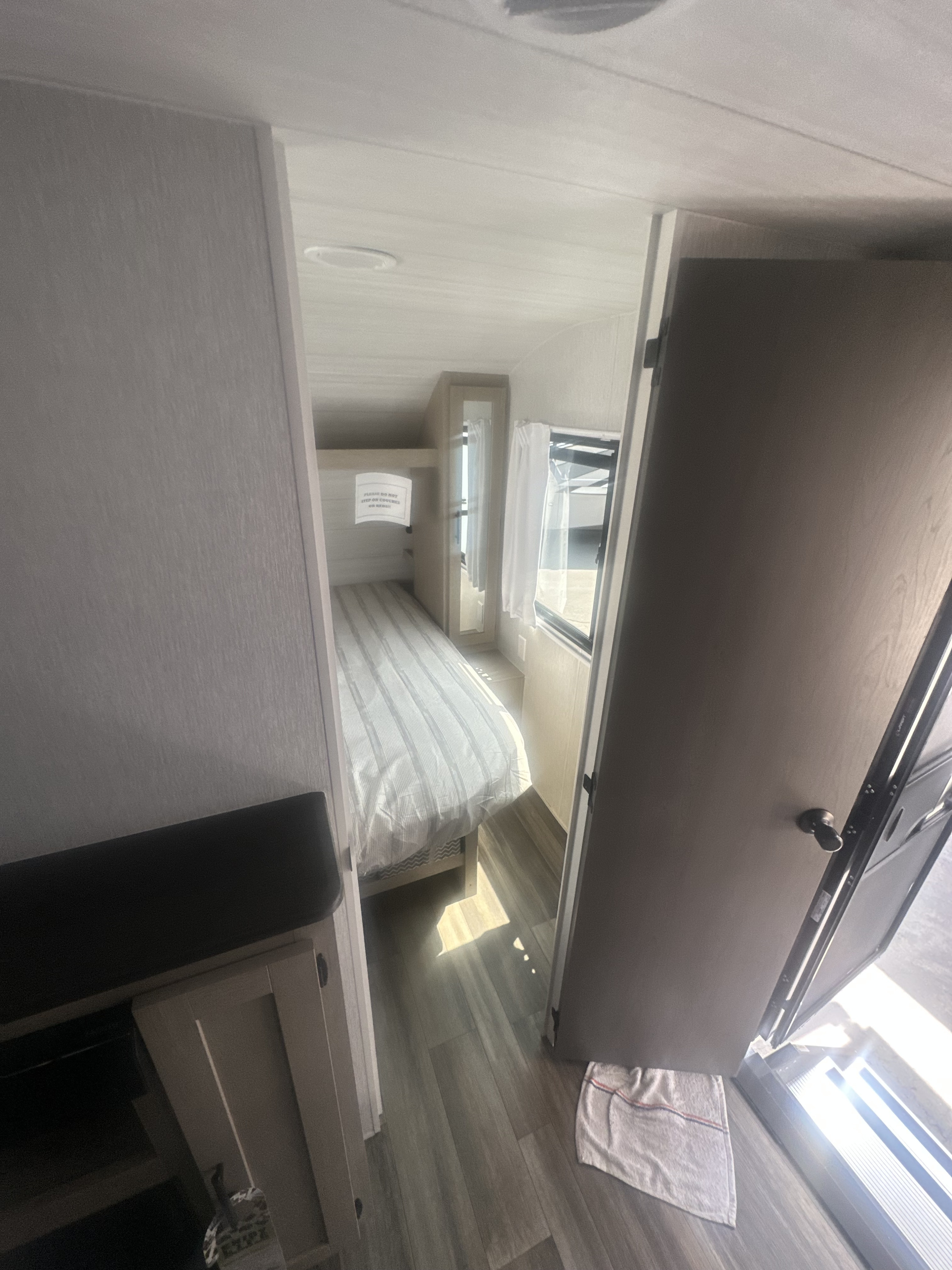 RV rental interior: bunk beds with striped bedding, a "do not step" sign, window, and open door.. Forest River Evo 2400bhl 2024
