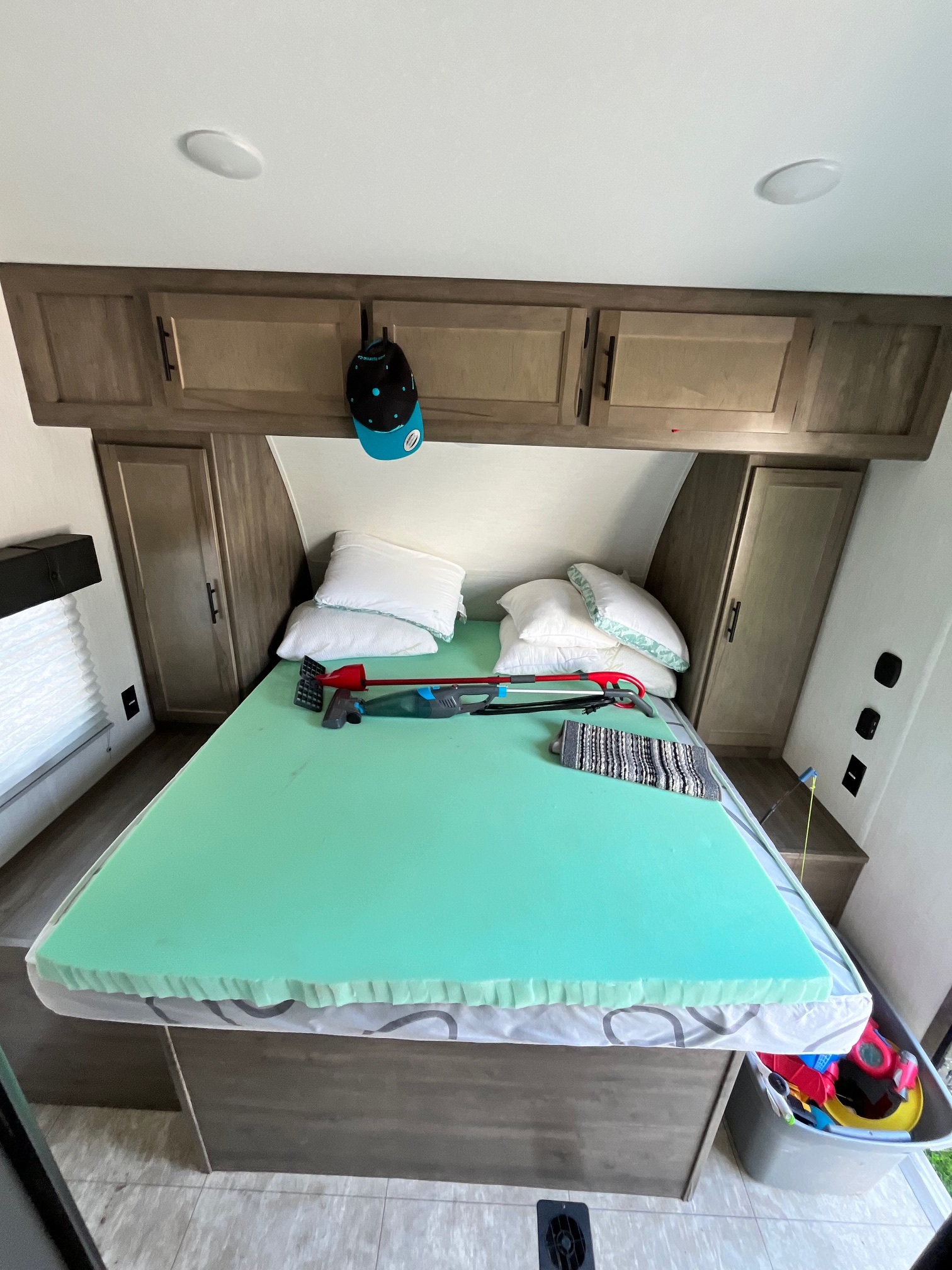 An RV rental bedroom features a bed with a vibrant green foam topper, pillows, overhead cabinets, and a bin of toys below.. Forest River Vengeance 2022