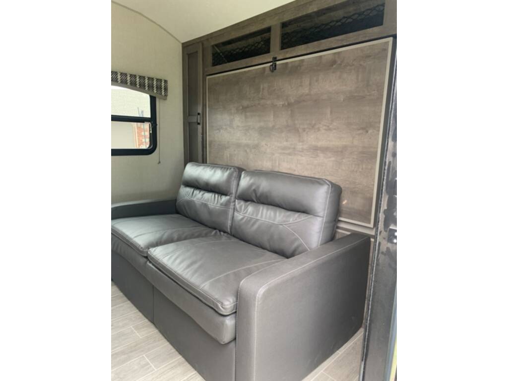 RV rental interior with a grey sofa and wall-mounted murphy bed, optimizing space for comfort and versatility.. Sonic Lite 2021