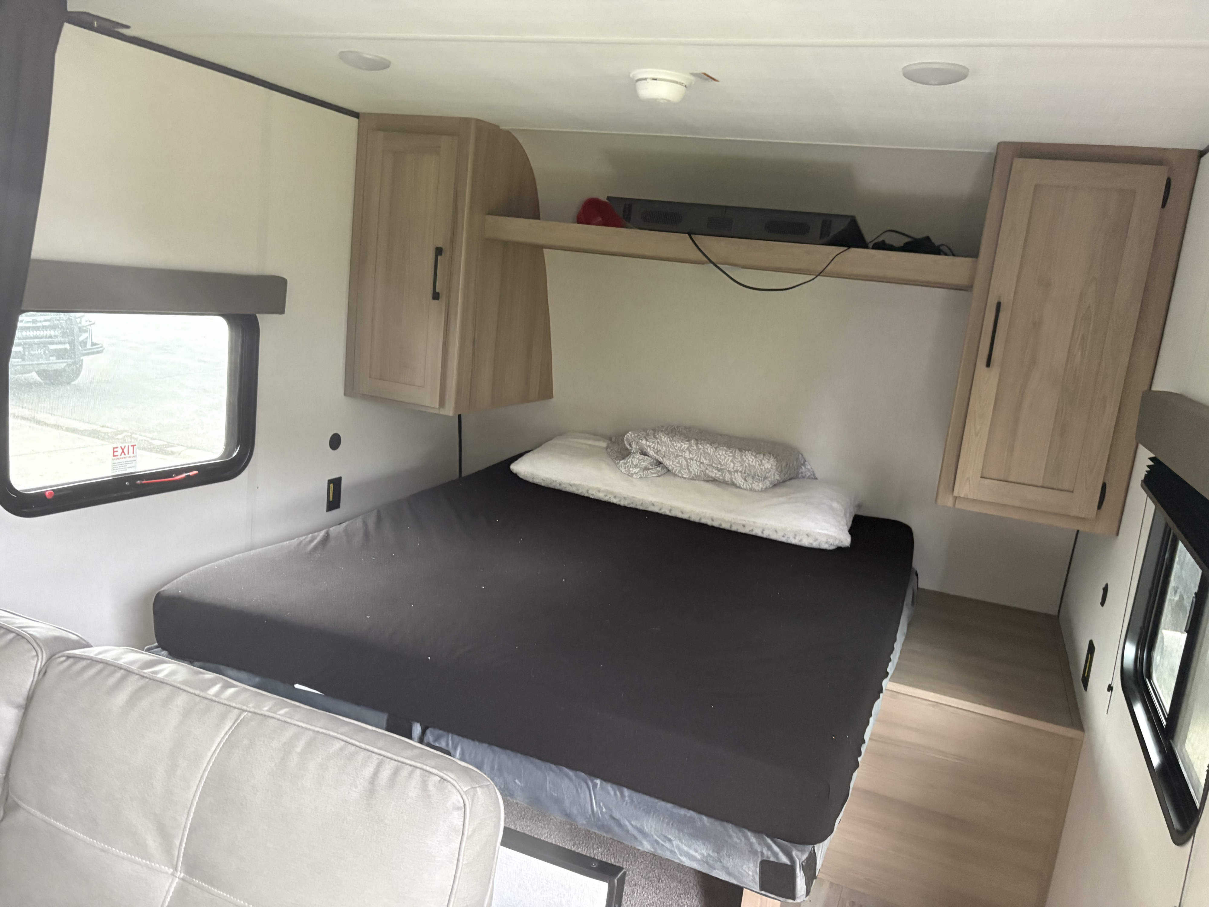 RV rental bedroom with dark mattress, overhead shelf and TV, light wood cabinets, and windows for travel.. Coleman 23B 2025