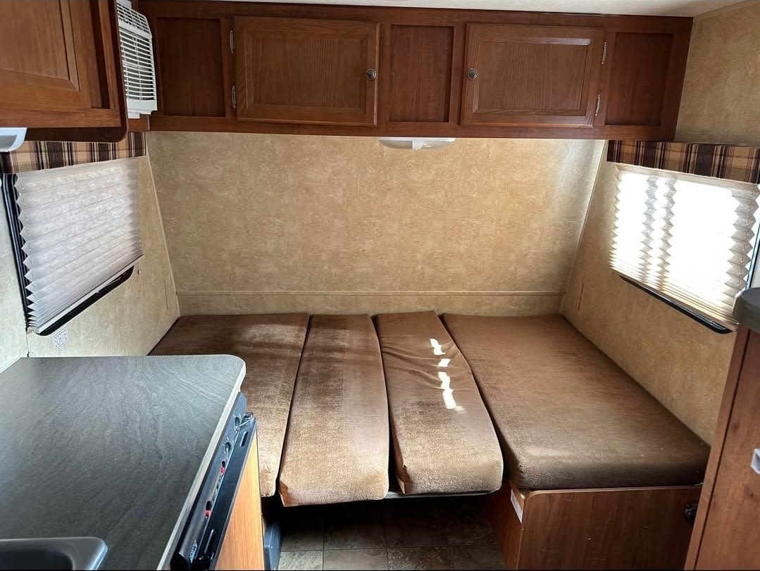 Inside an RV rental: a compact living space featuring brown bench seating, overhead wood cabinets, and a small kitchen prep area.. Jayco Jay Flight Swift SLX 2012