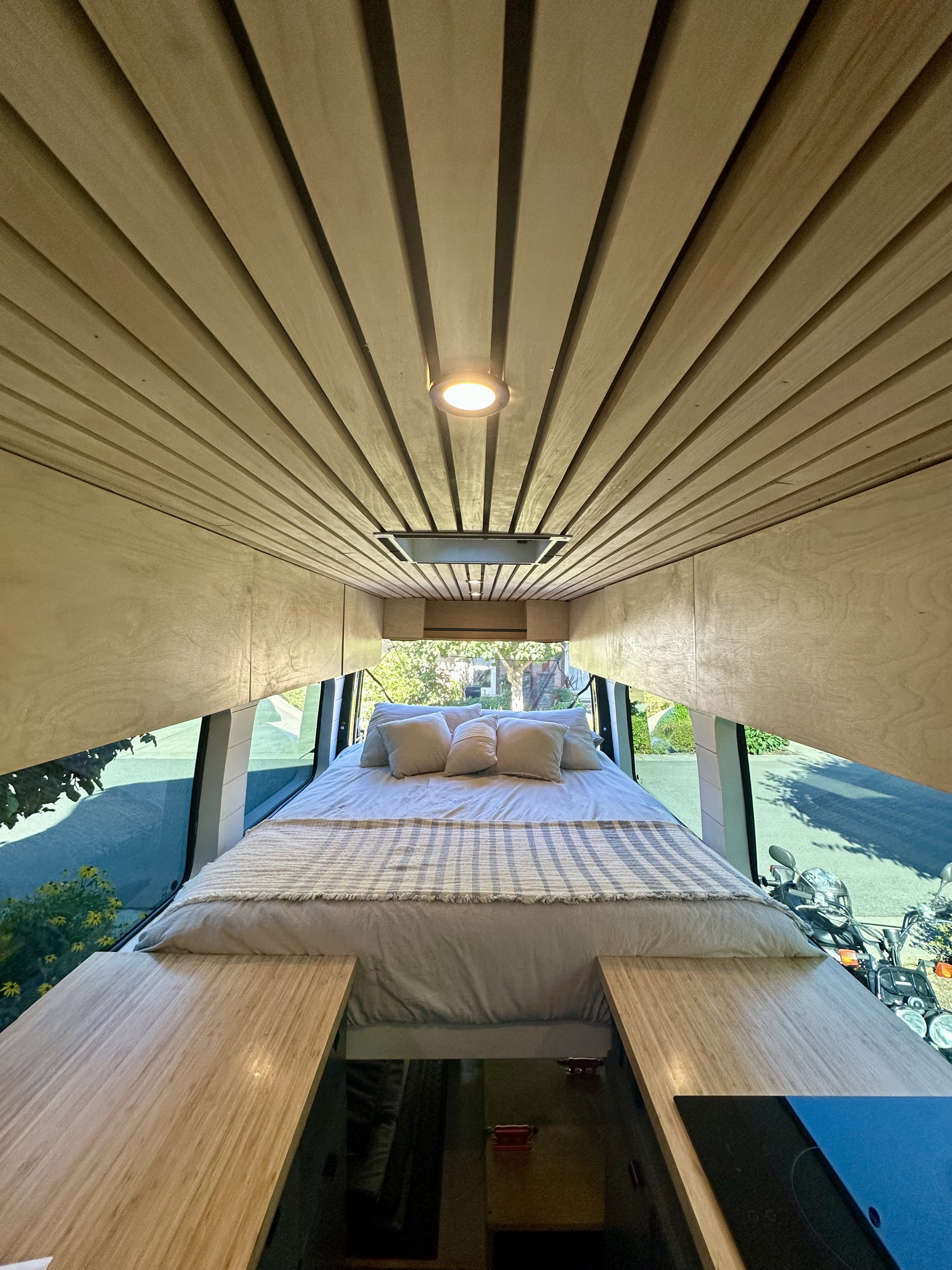 Well-appointed RV rental interior with a cozy bed, slatted wood ceiling, and panoramic window views.. Mercedes Sprinter 2007