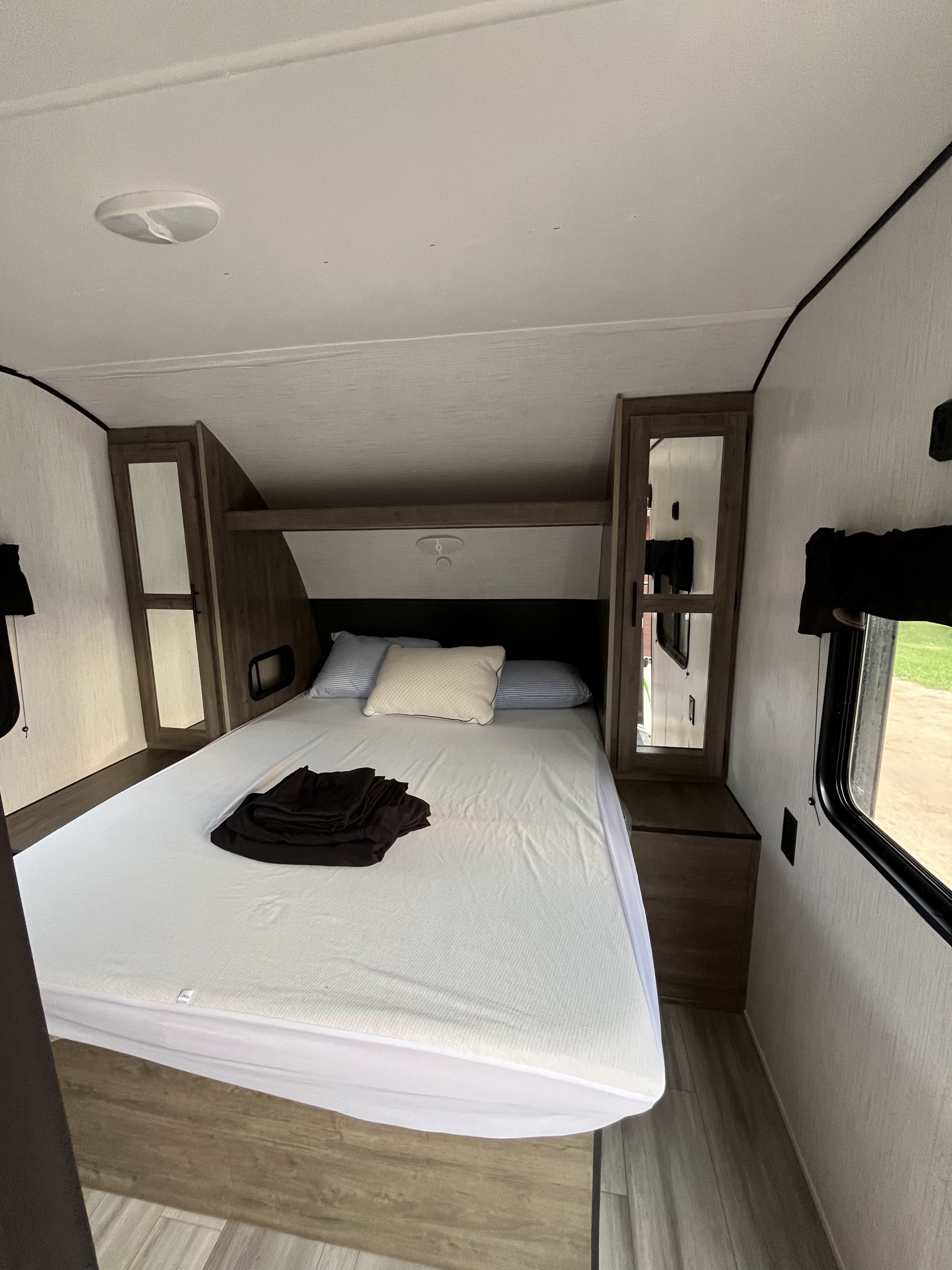 Clean RV rental bedroom featuring a queen bed with white bedding, mirrored cabinets, and light wood flooring.. Heartland RVs Pioneer 2022