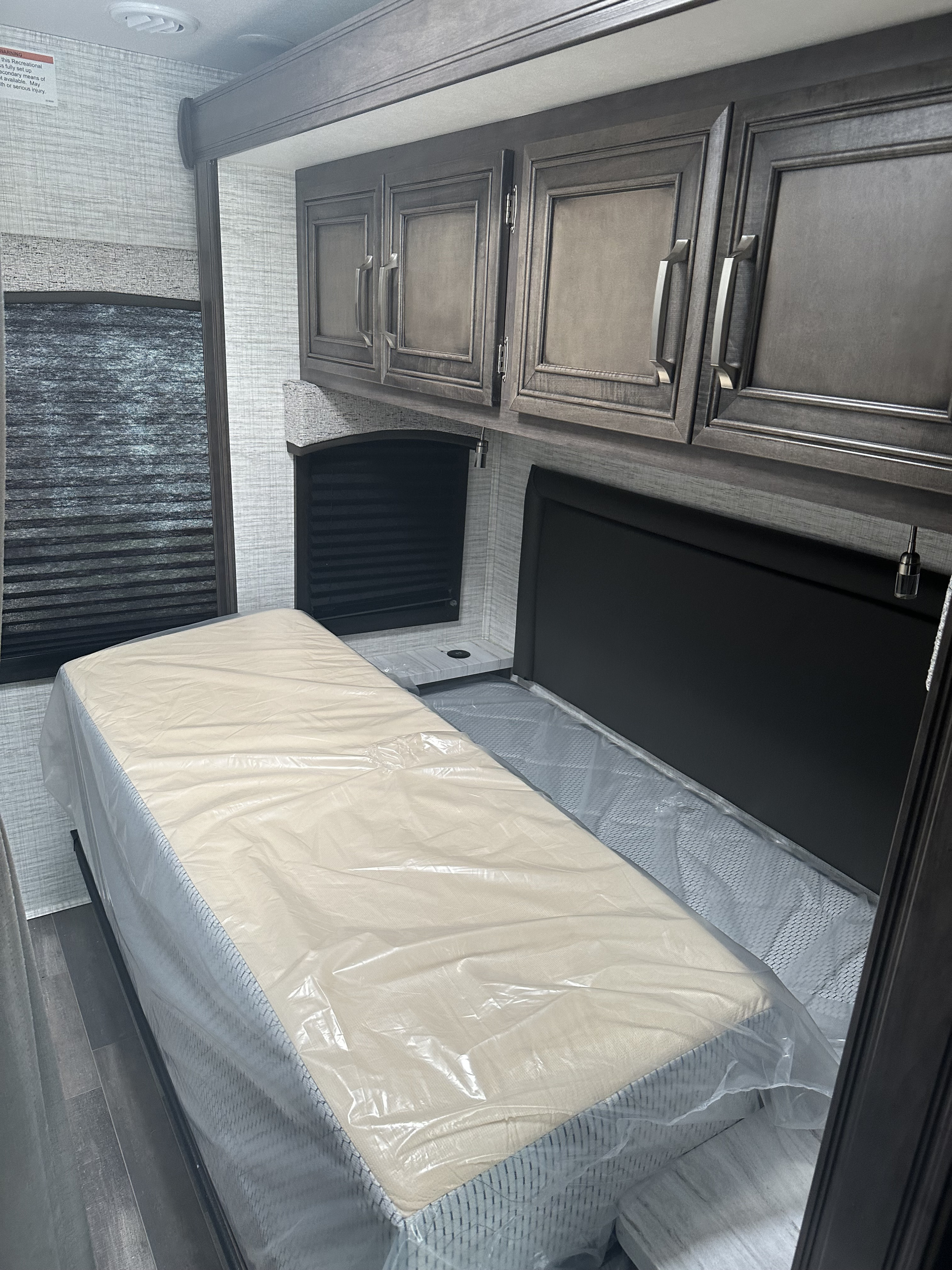 RV rental bedroom featuring a new, plastic-wrapped mattress, dark cabinets, and a window. Clean and ready.. Entegra Coach Odyssey SE 2024