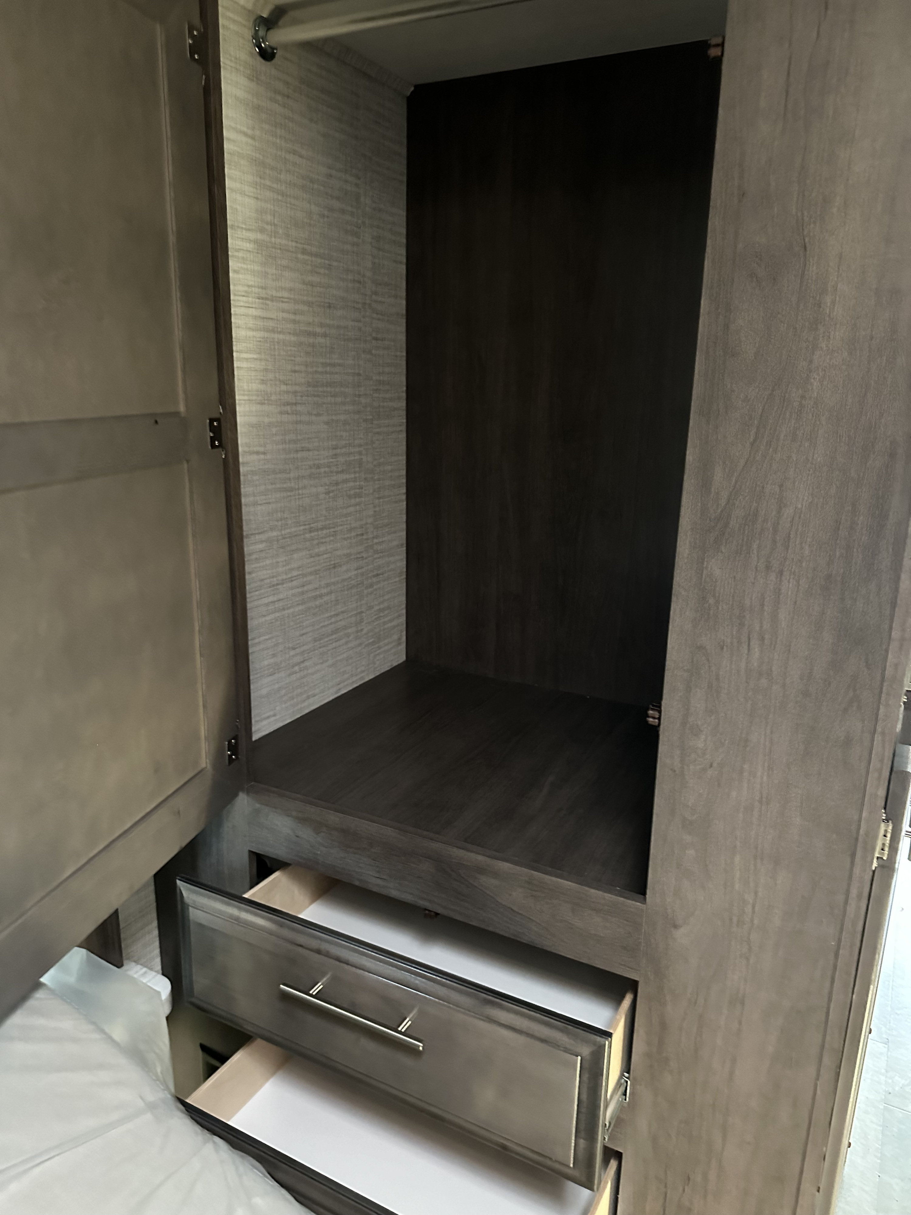 RV rental interior: Open wardrobe with hanging space, shelf, and pull-out drawers for bedroom storage.. Entegra Coach Odyssey SE 2024