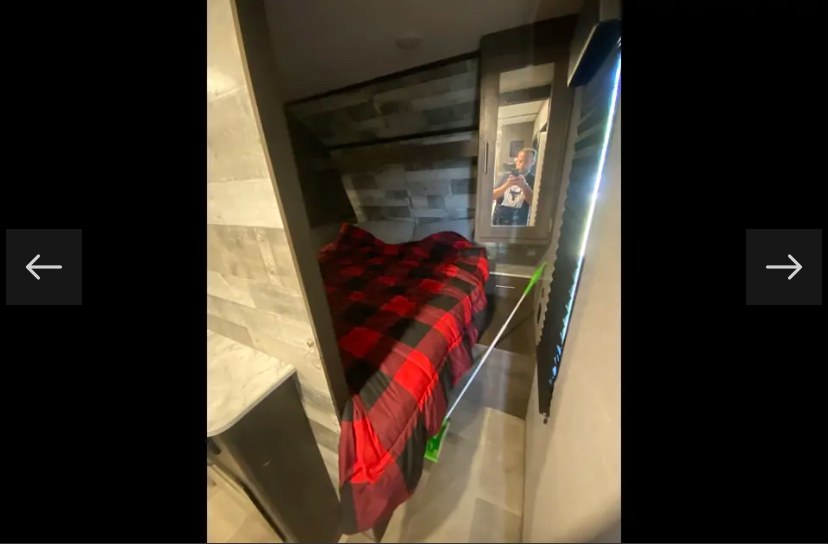 Explore this cozy RV rental's bedroom, featuring a red plaid bed, built-in shelves, and a mirrored closet door.. Coachmen Lantern 2021
