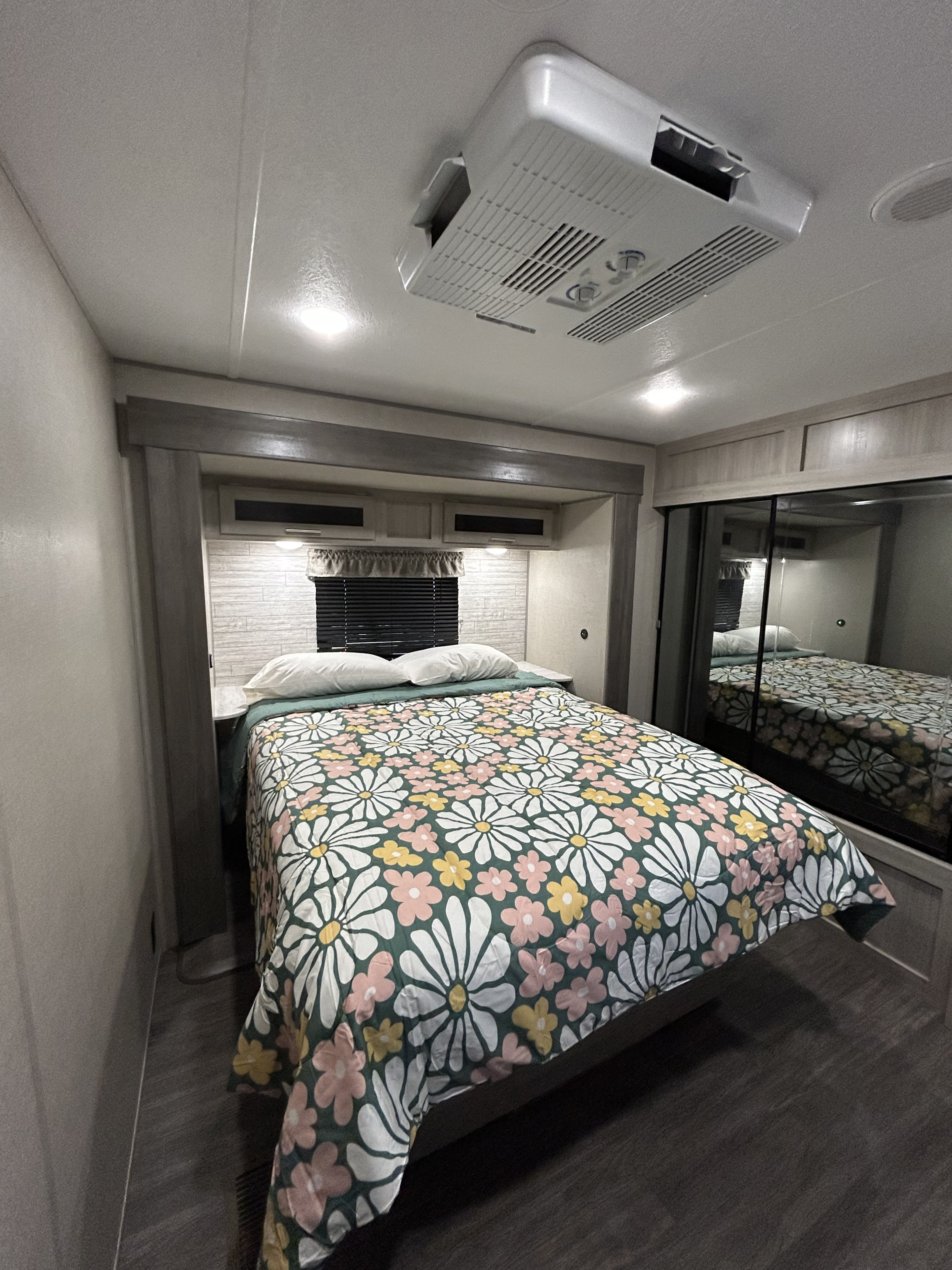 Cozy RV rental bedroom featuring a bed with a vibrant daisy-patterned comforter, mirrored closet, and overhead AC unit.. Forest River Aurora Aurora 2023