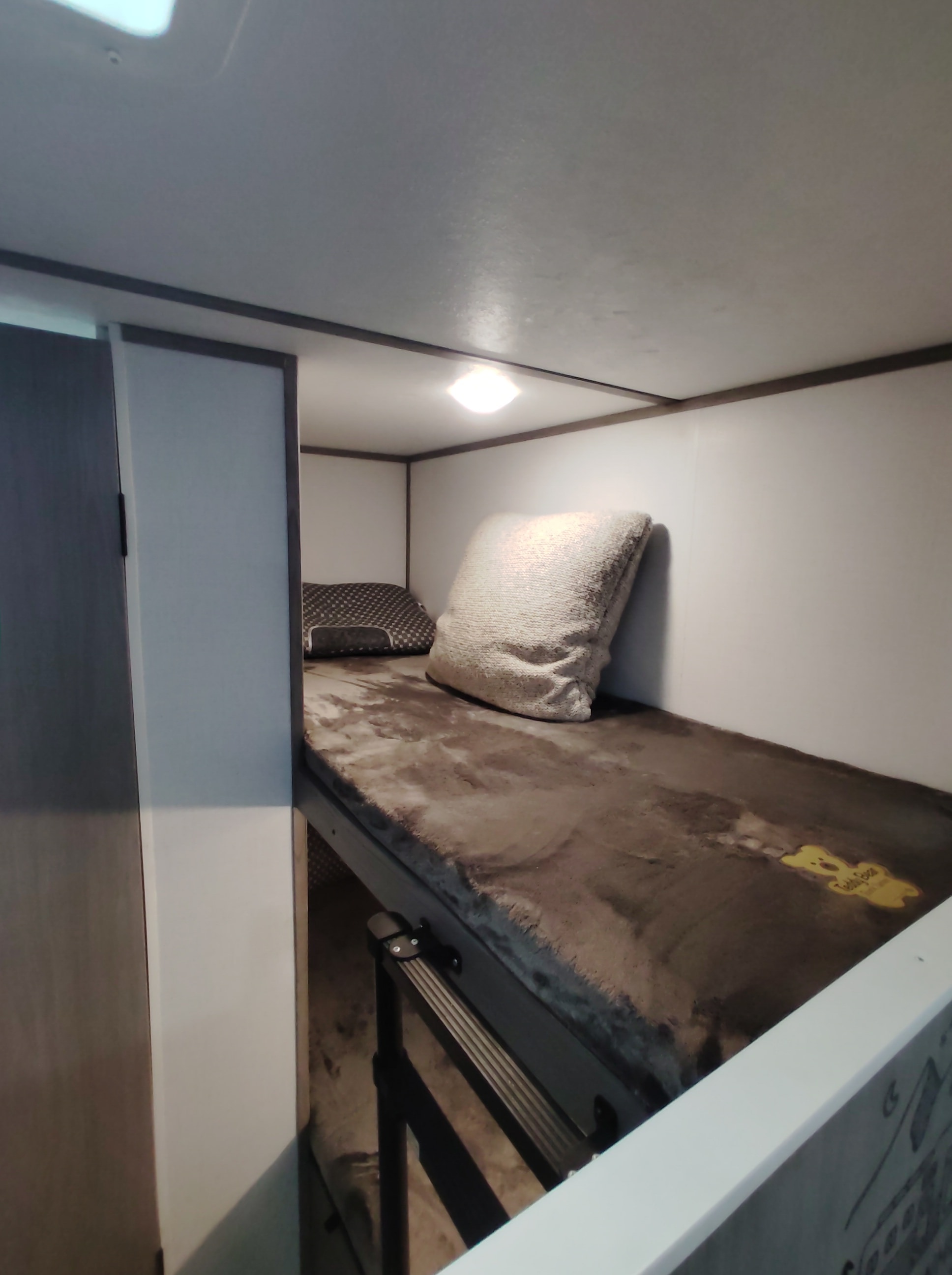 Cozy bunk bed in an RV rental, featuring a plush blanket, two pillows, and an overhead light. Ideal for compact sleeping.. Dutchmen 17B 2024