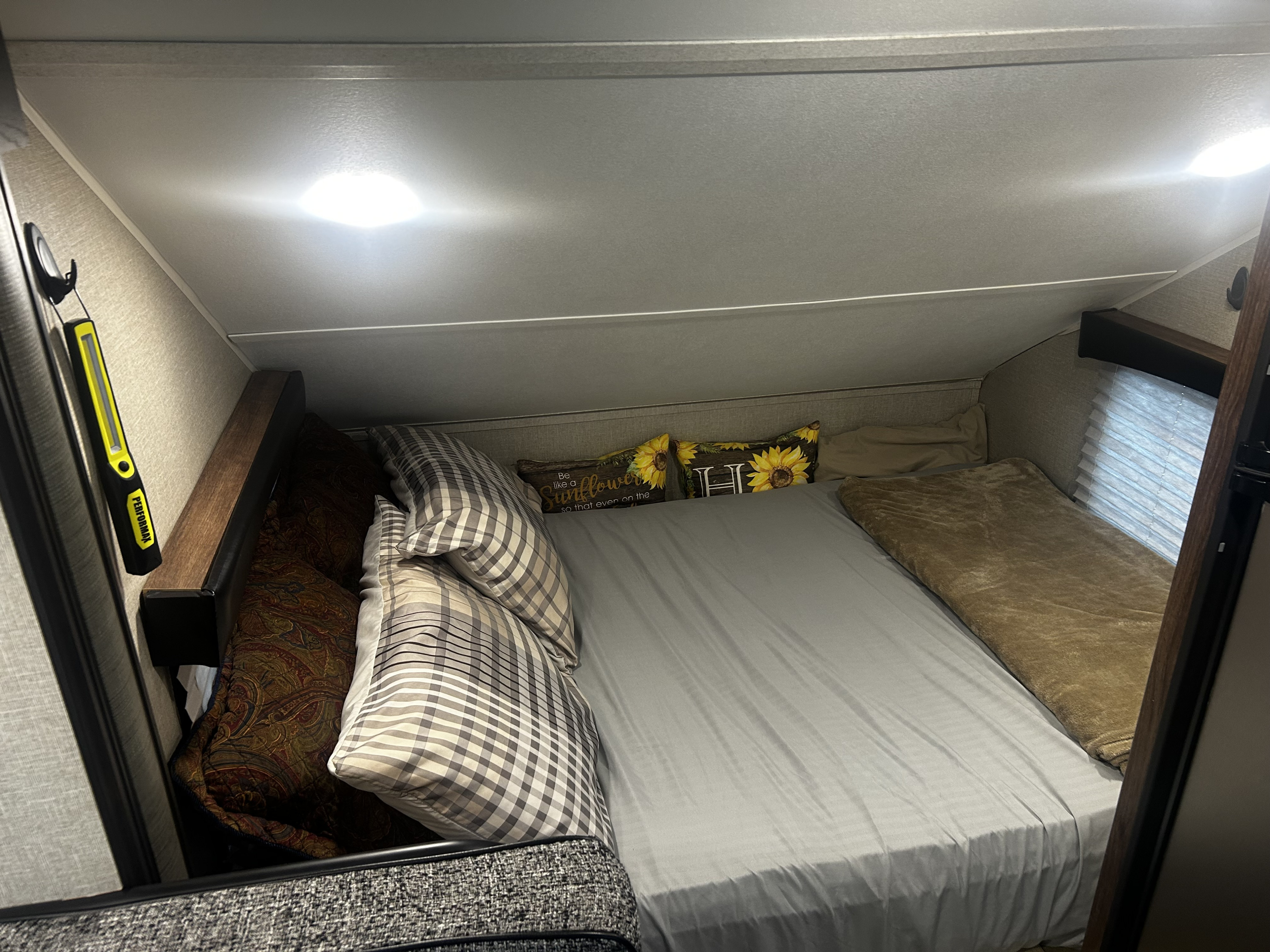 Experience comfort in this RV rental's cozy bedroom. Features include a bed with sunflower pillows & overhead lighting.. Travel Lite Falcon 2018