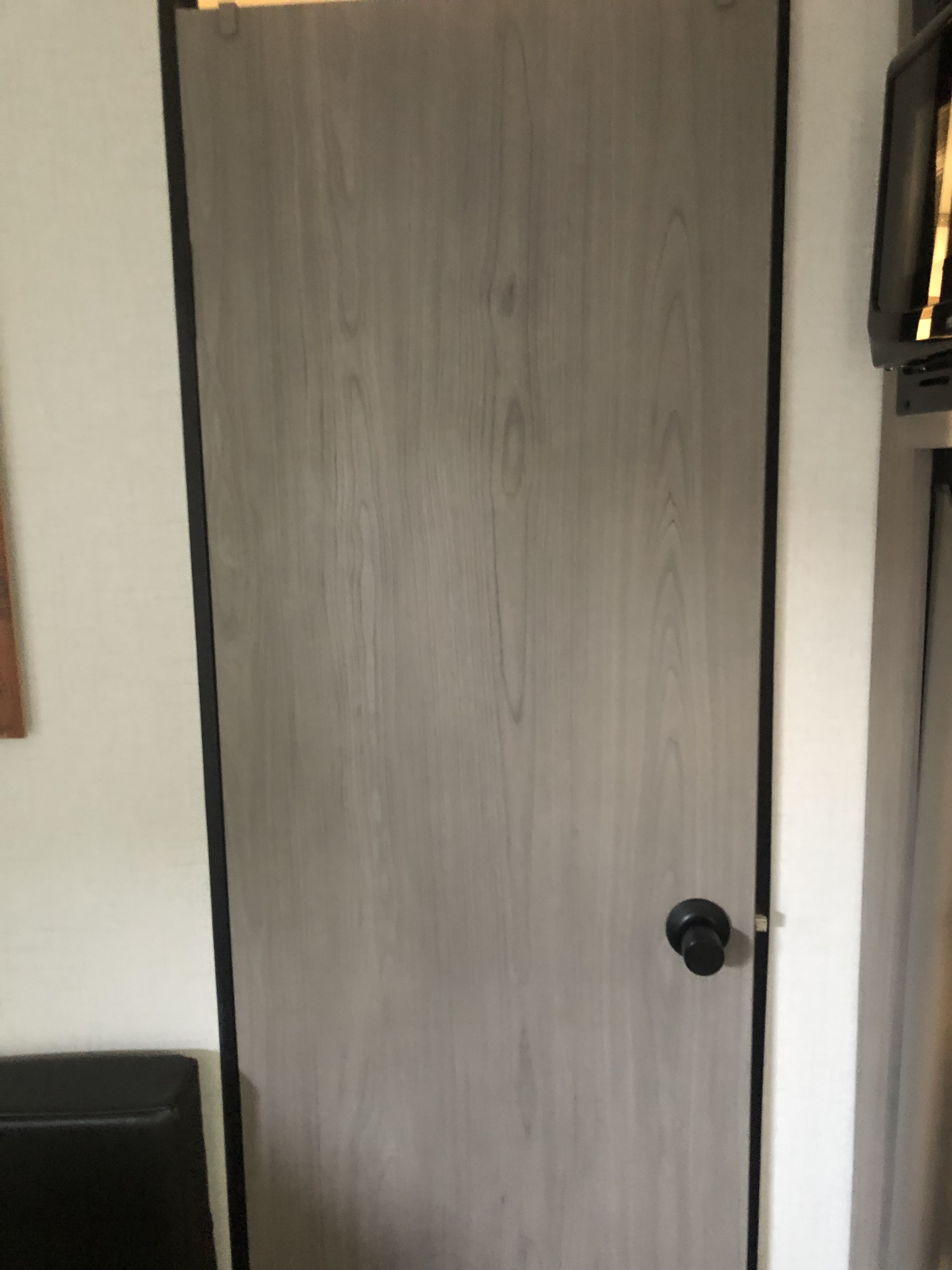 A light gray, wood-grain patterned interior door with a black knob, typical for an RV rental.. Coleman Lantern 17R 2024