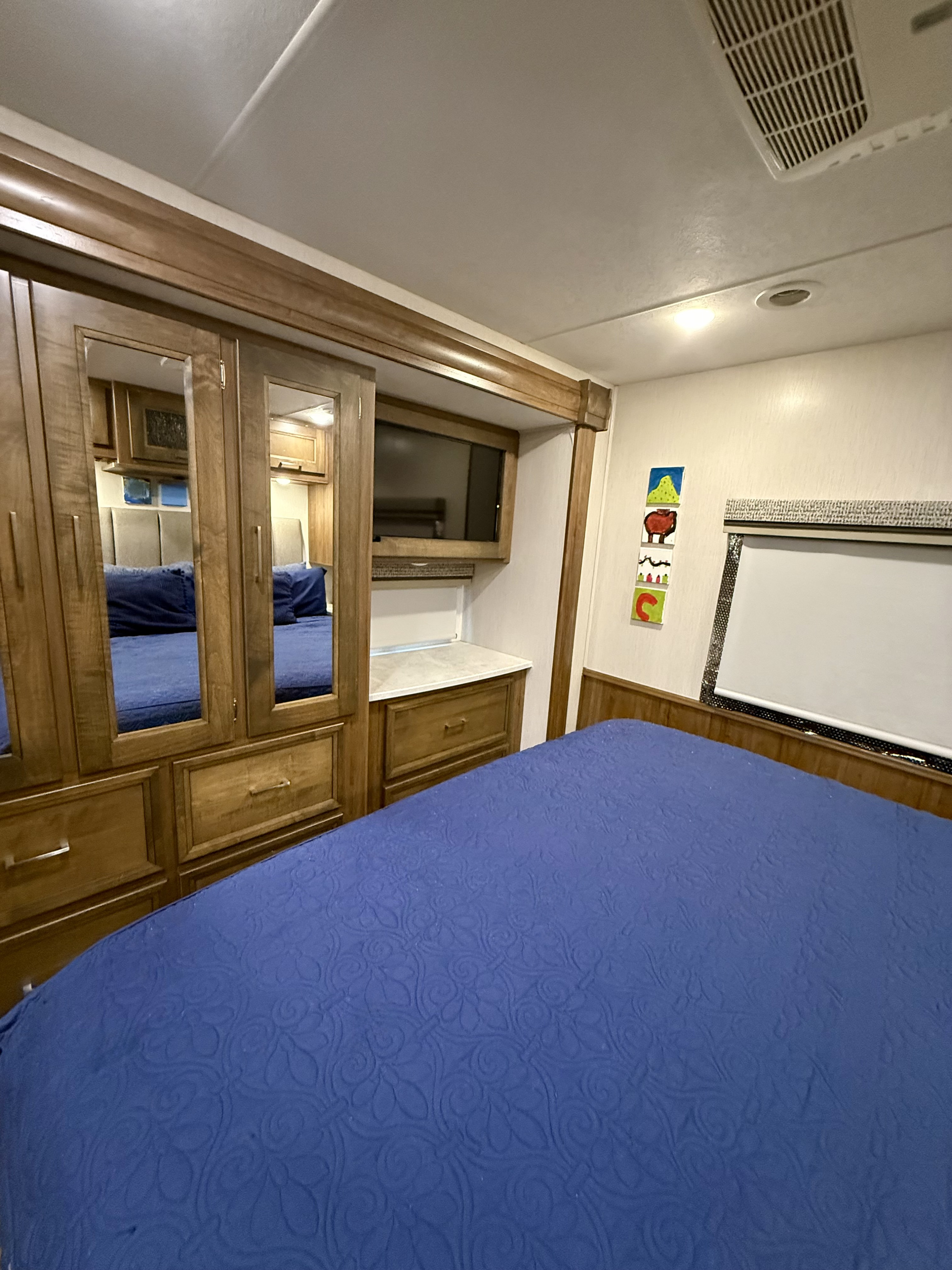 Cozy RV rental bedroom featuring a blue bed, mirrored wooden cabinetry, TV, and AC unit for comfortable travel.. Coachmen Mirada 2020