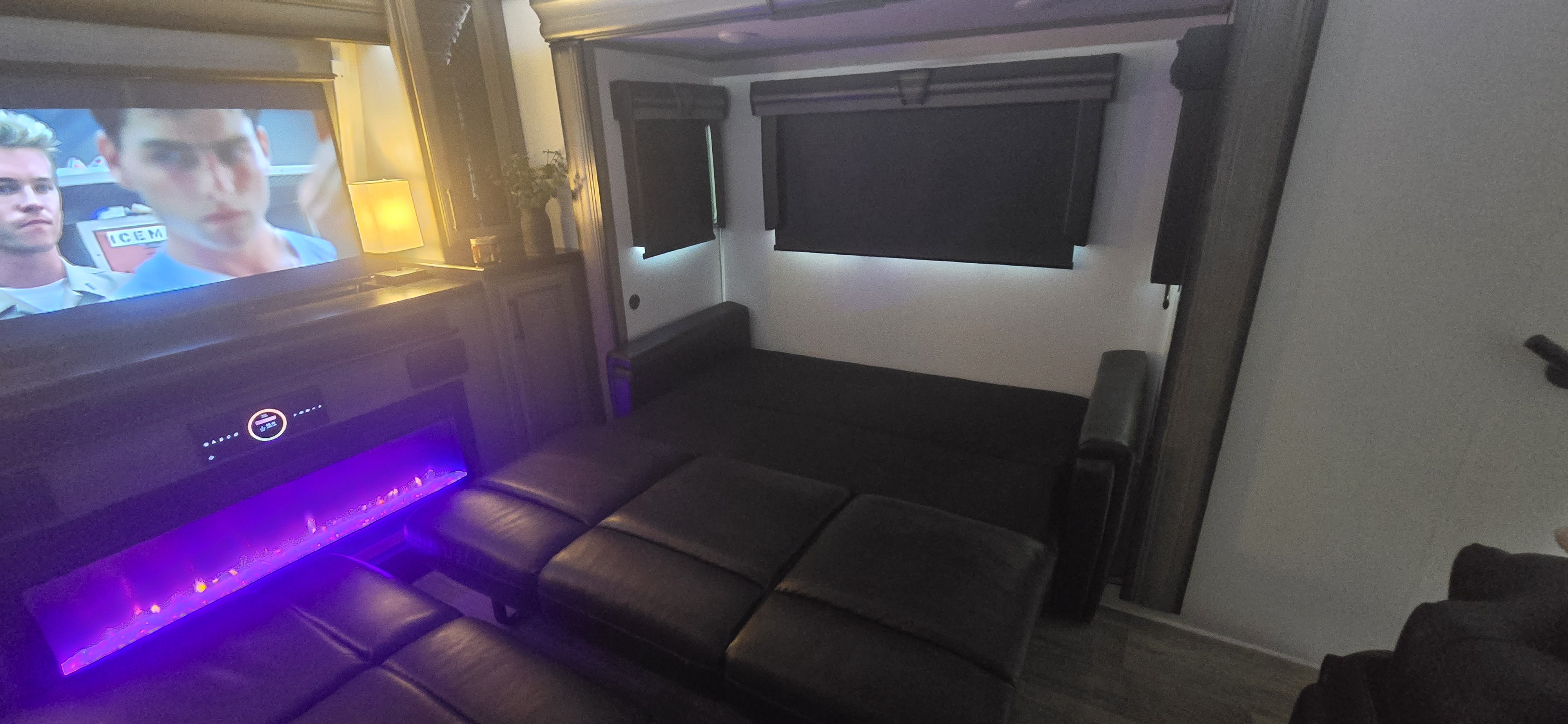 Cozy RV rental interior: TV, purple-lit electric fireplace, and dark pull-out sofa bed for relaxing.. Keystone RV Montana 2023