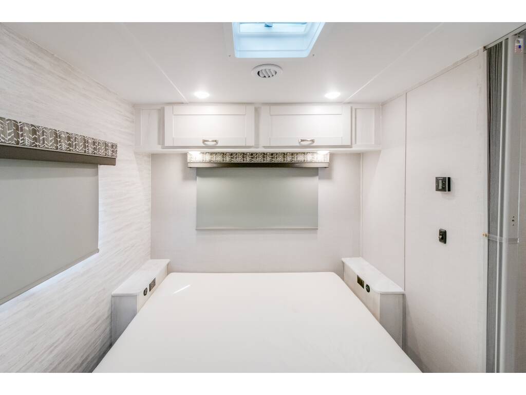 RV rental bedroom with white decor, featuring bed, overhead cabinets, skylight & side controls.. Gulf Stream Conquest 2023