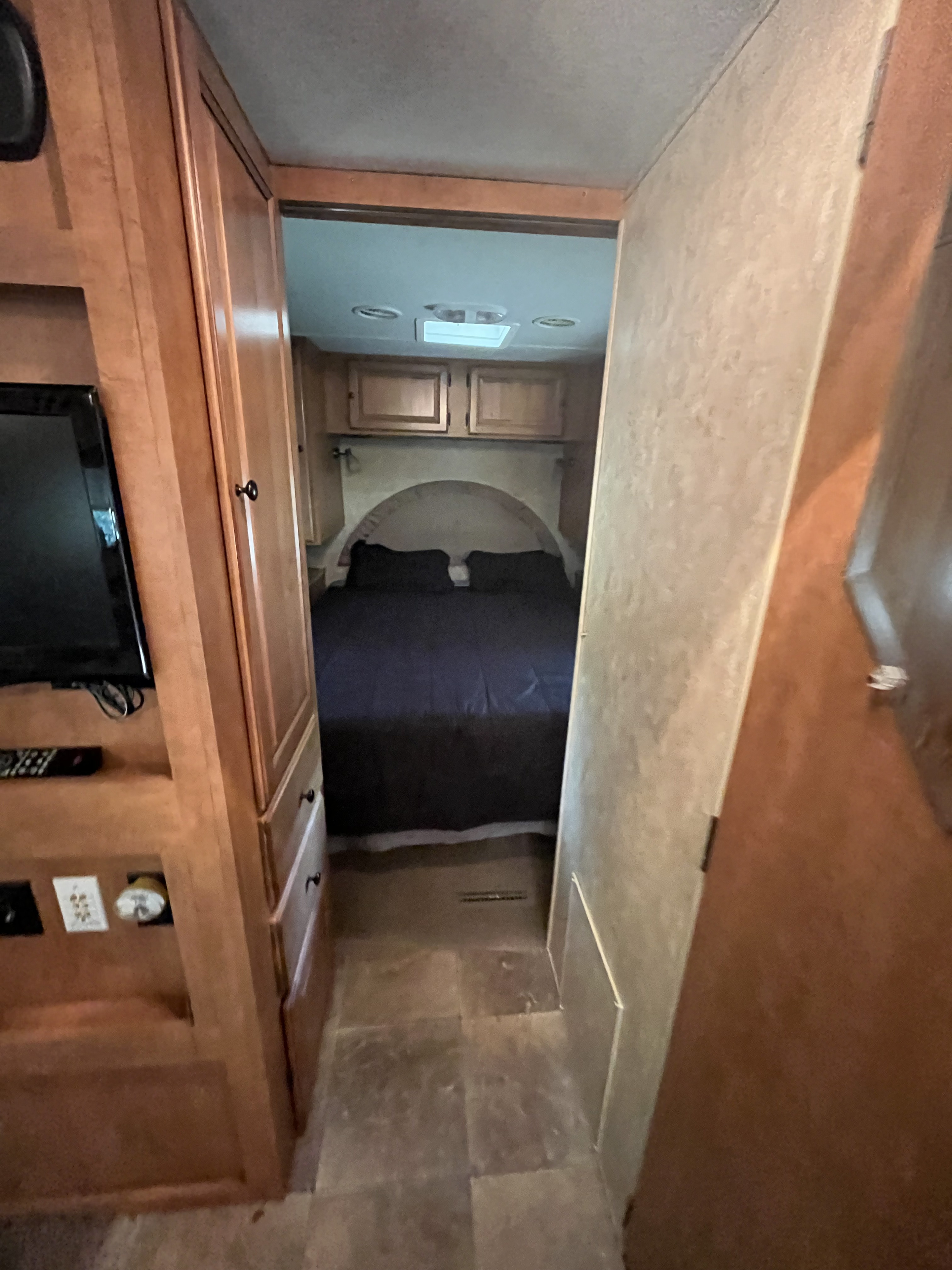 Experience this RV rental's cozy bedroom, visible from a wood-paneled hallway. Features dark bedding, arched headboard, and cabinets.. Forest River Palomino Thoroughbred Elite 2012