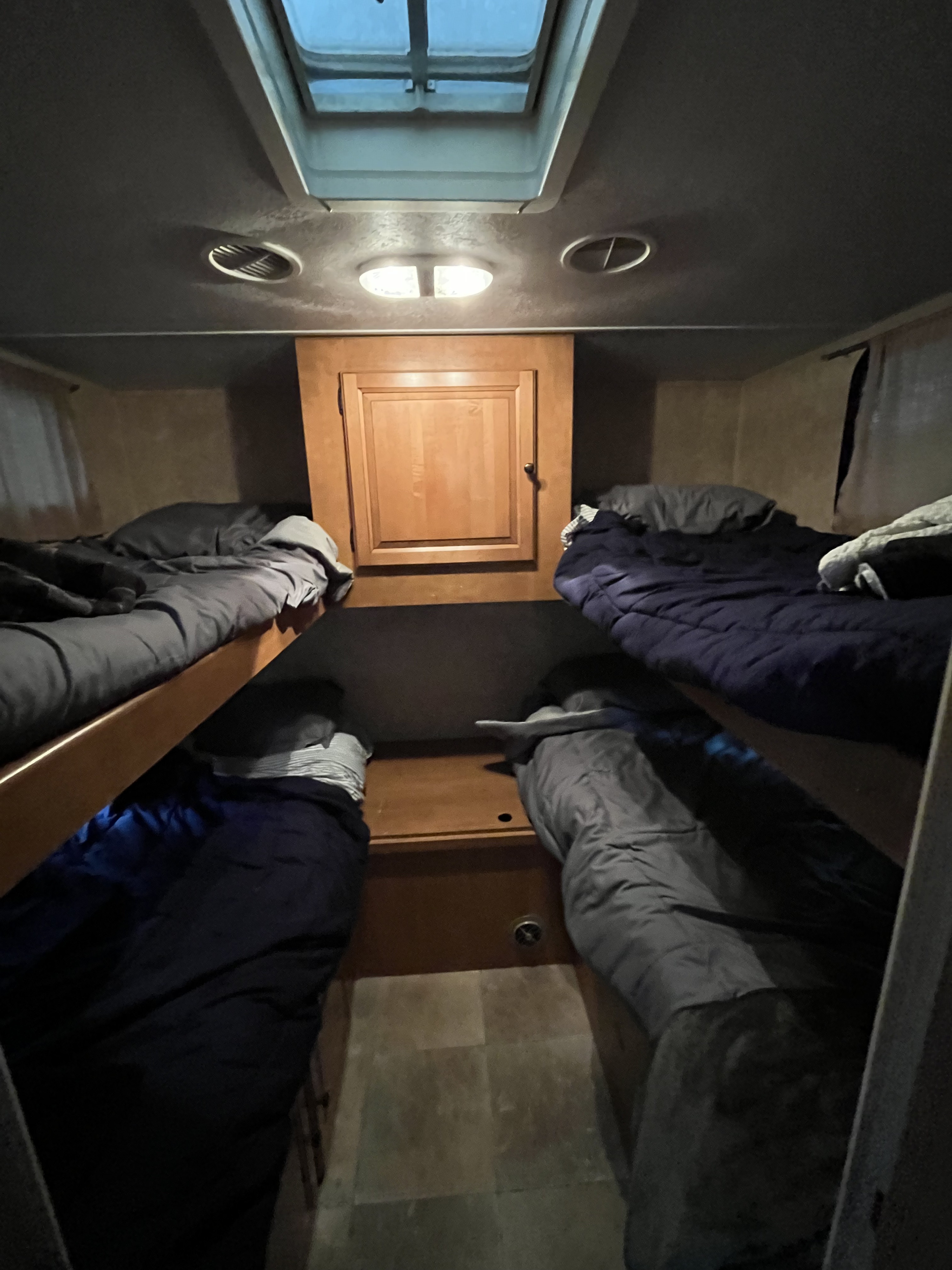 Inside an RV rental: two sets of bunk beds with bedding, ready for guests. A central cabinet and ceiling lights are visible.. Forest River Palomino Thoroughbred Elite 2012