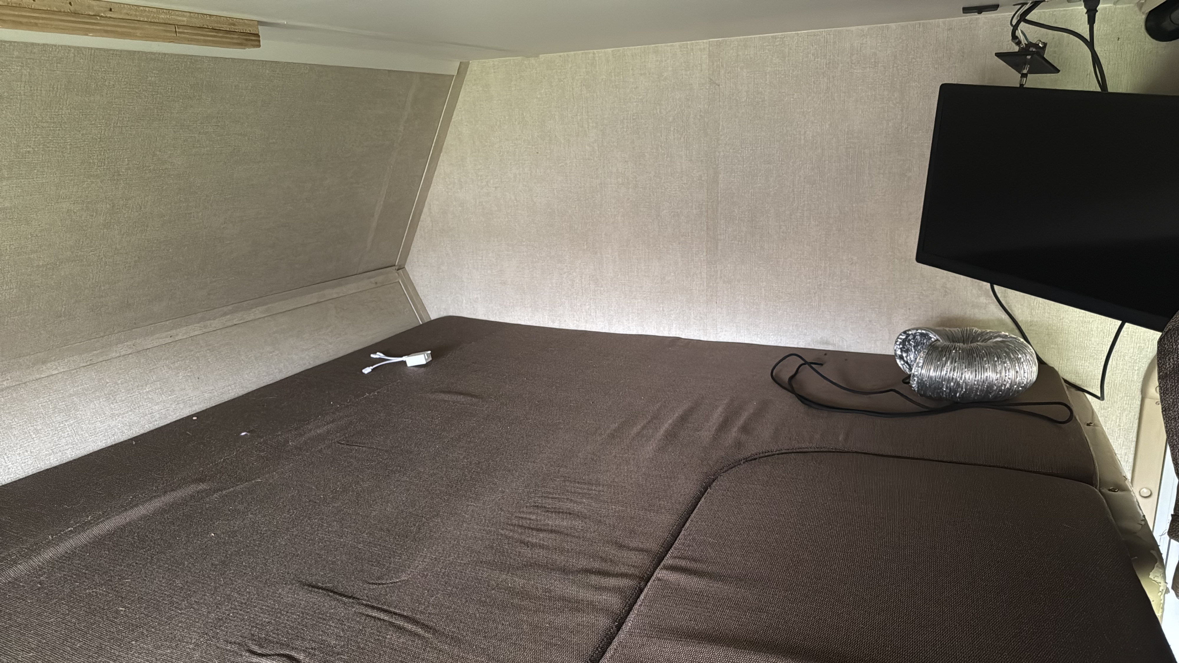 View inside an RV rental showing a brown mattress, wall-mounted TV, and flexible duct. Simple comfort for travel.. Gulf Stream Conquest 2017