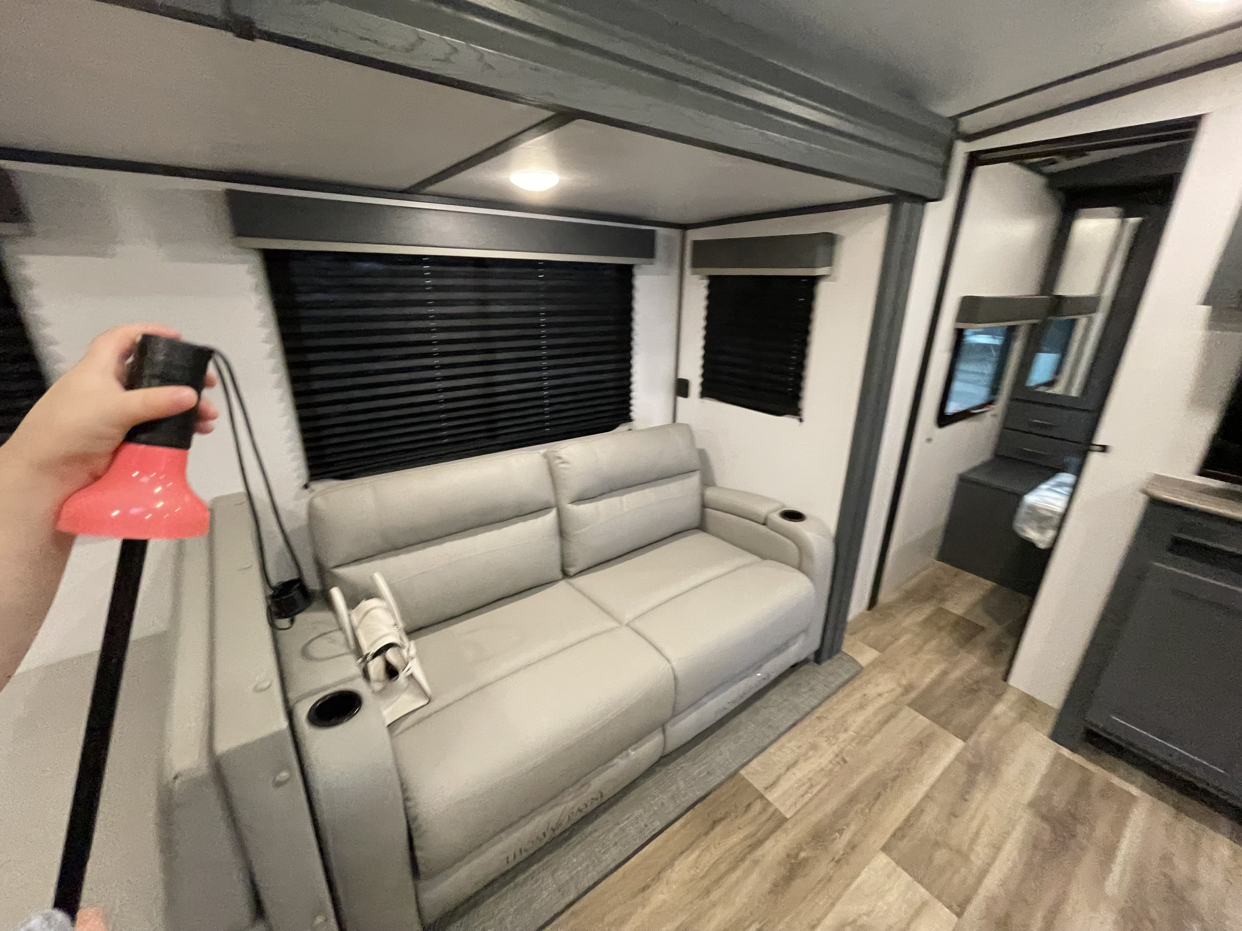 Modern RV interior featuring a light gray reclining sofa, dark blinds, and wood-look flooring, great for your RV rental.. Keystone RV Bullet Ultra Lite 2022
