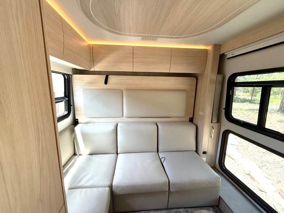 Modern RV rental interior: Light wood, modular sofa, and bright lighting create a comfy travel space.. Leisure Travel Vans Unity 2022