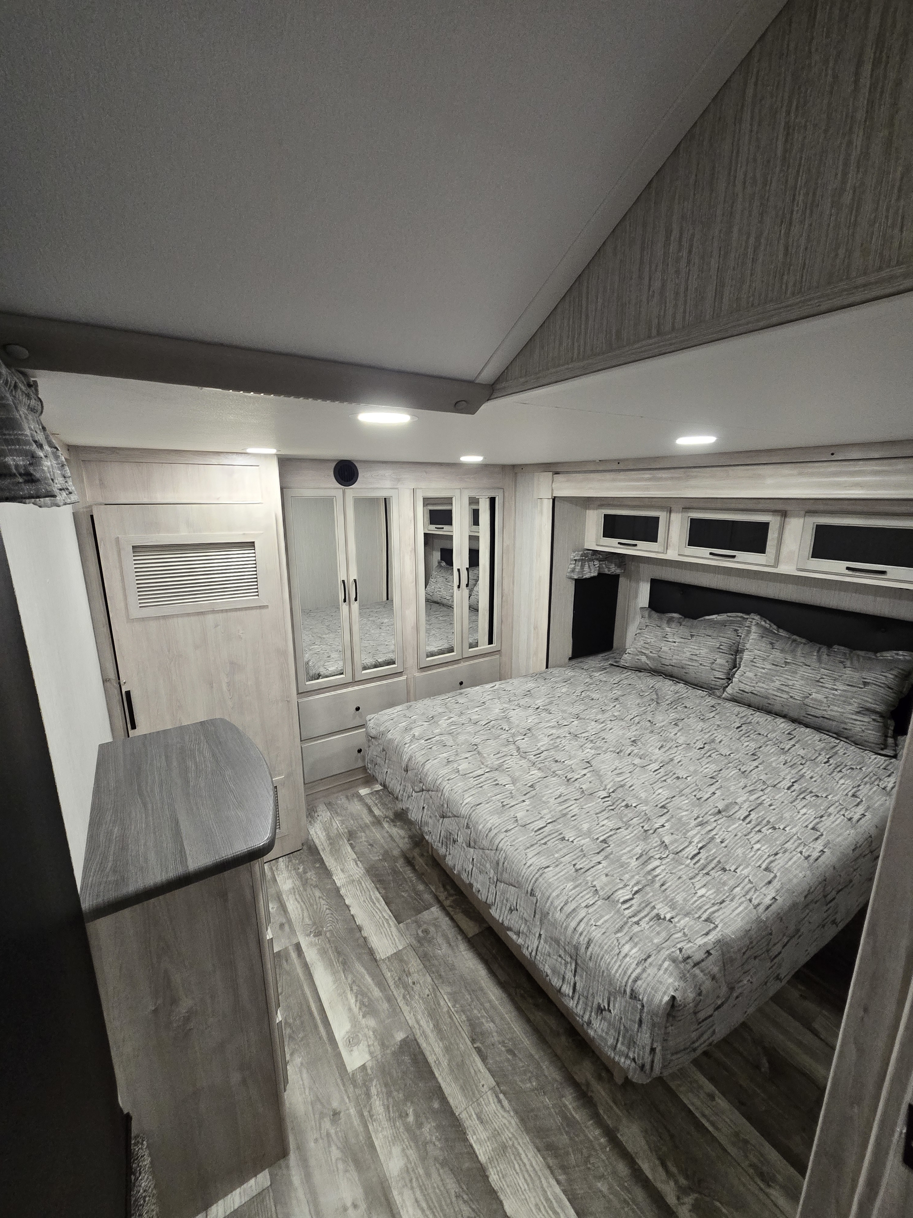Spacious, modern RV rental bedroom featuring a large bed, mirrored wardrobe, overhead cabinets, and wood-look flooring.. Forest River Sandpiper 2023
