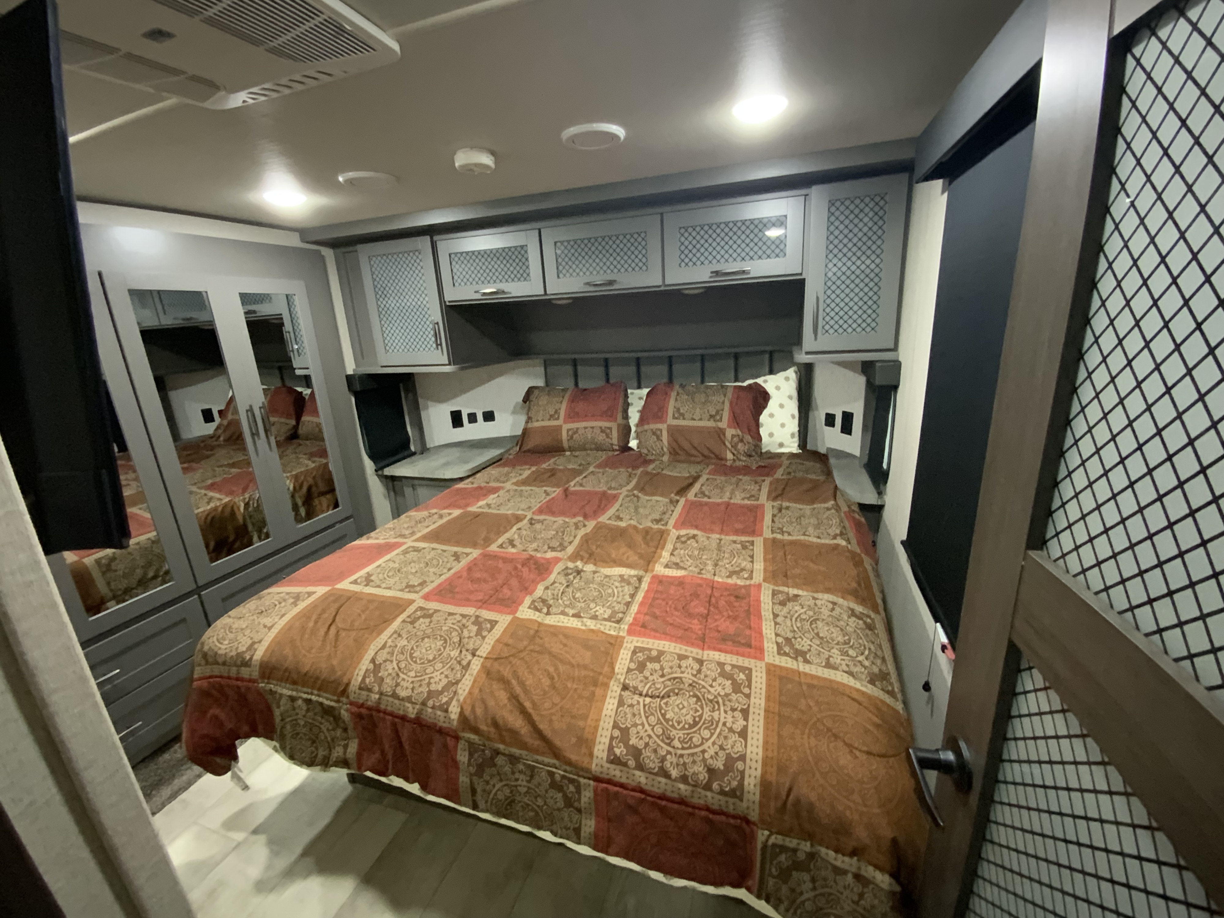 Spacious bedroom in an RV rental, featuring a cozy bed, ample storage cabinets, and mirrored closet doors.. Grand Design Momentum 2024