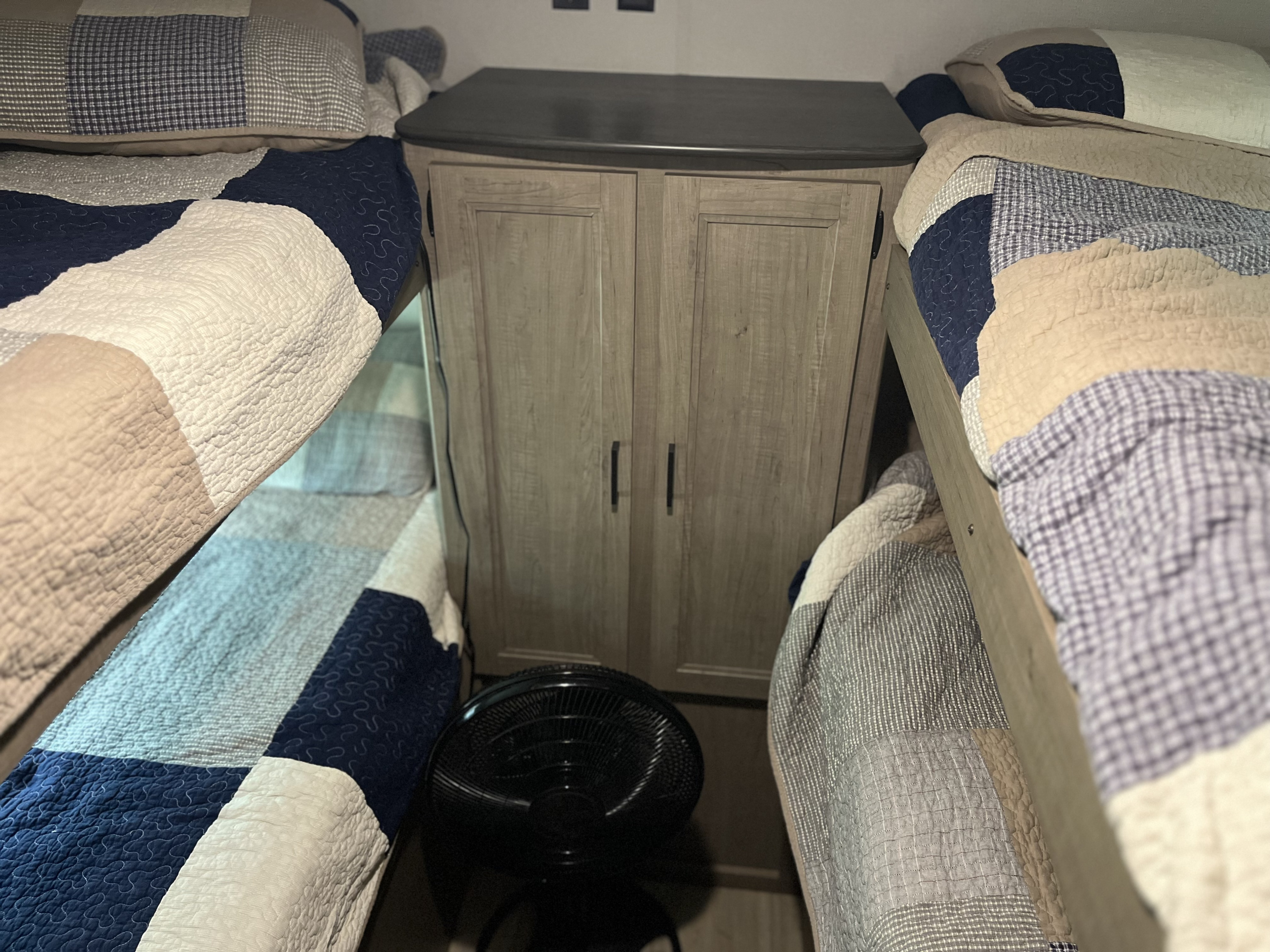 An RV rental interior shows two cozy bunk beds with patchwork quilts, a central storage cabinet, and a floor fan.. Keystone RV Hideout LHS 2020