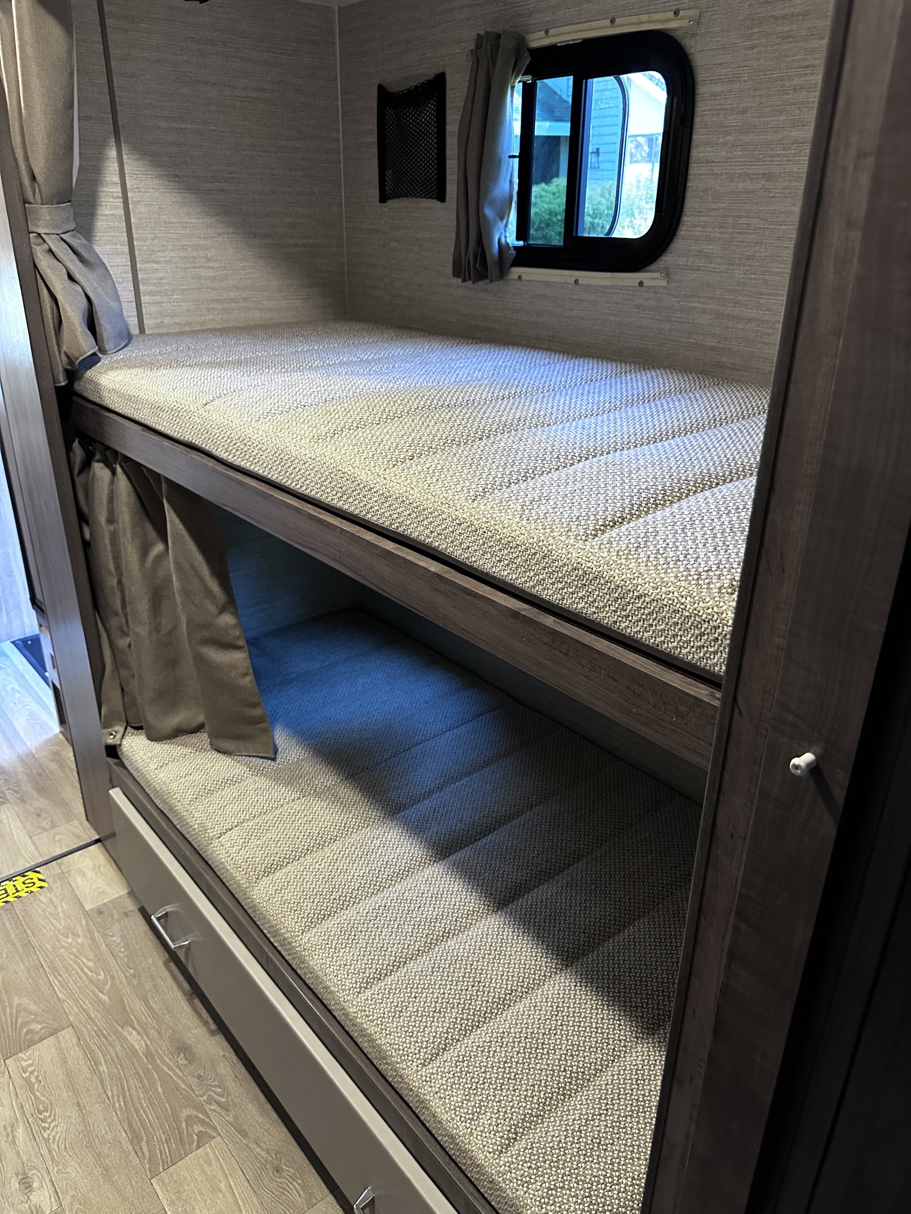 Inside this RV rental: two stacked bunk beds with textured mattresses, privacy curtains, and a window.. Winnebago Minnie Winnie 2026