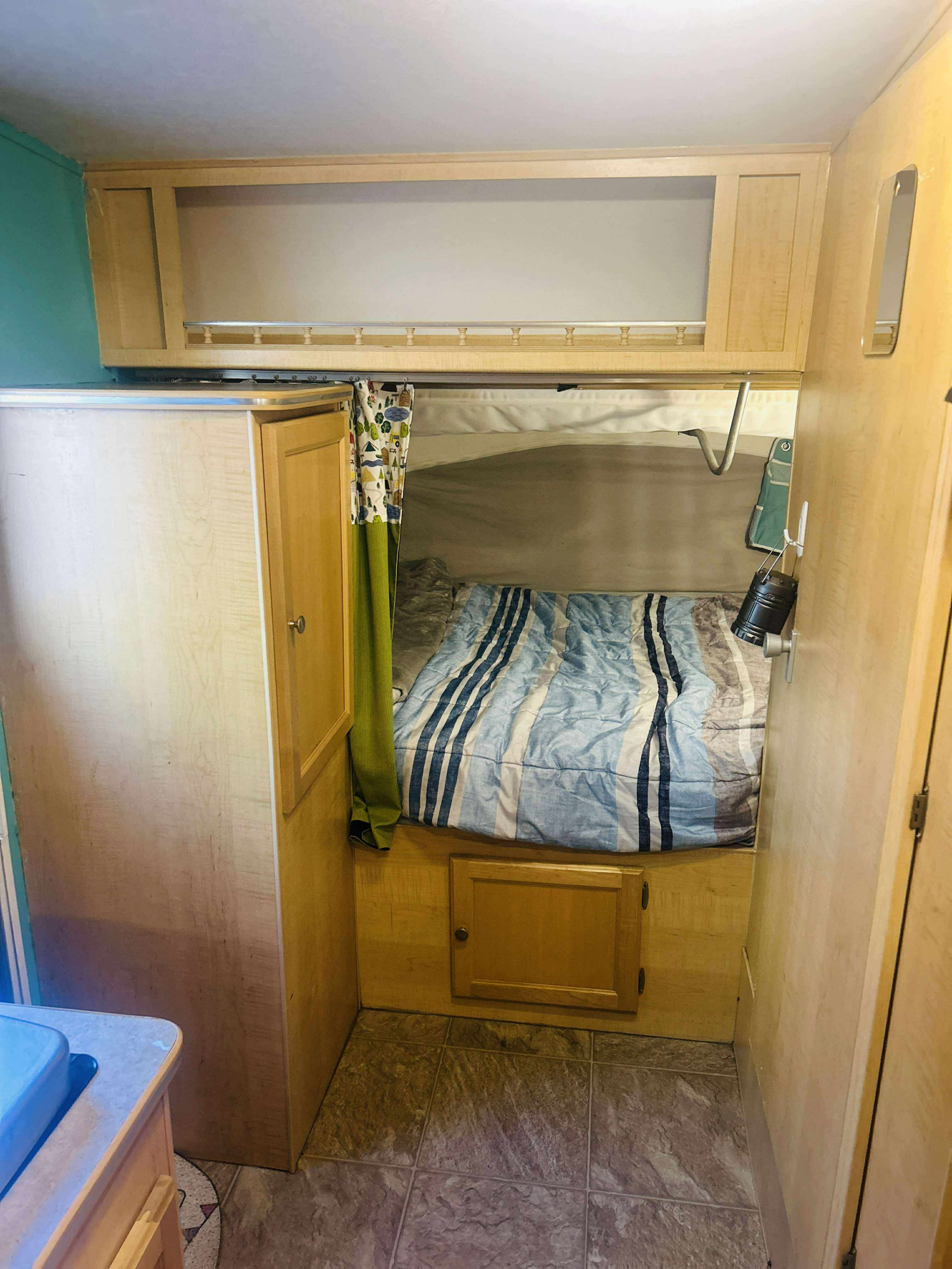 Compact RV rental bedroom with striped bed, wooden cabinets, and hanging lantern. Ideal for cozy travels.. Forest River M-17 2005