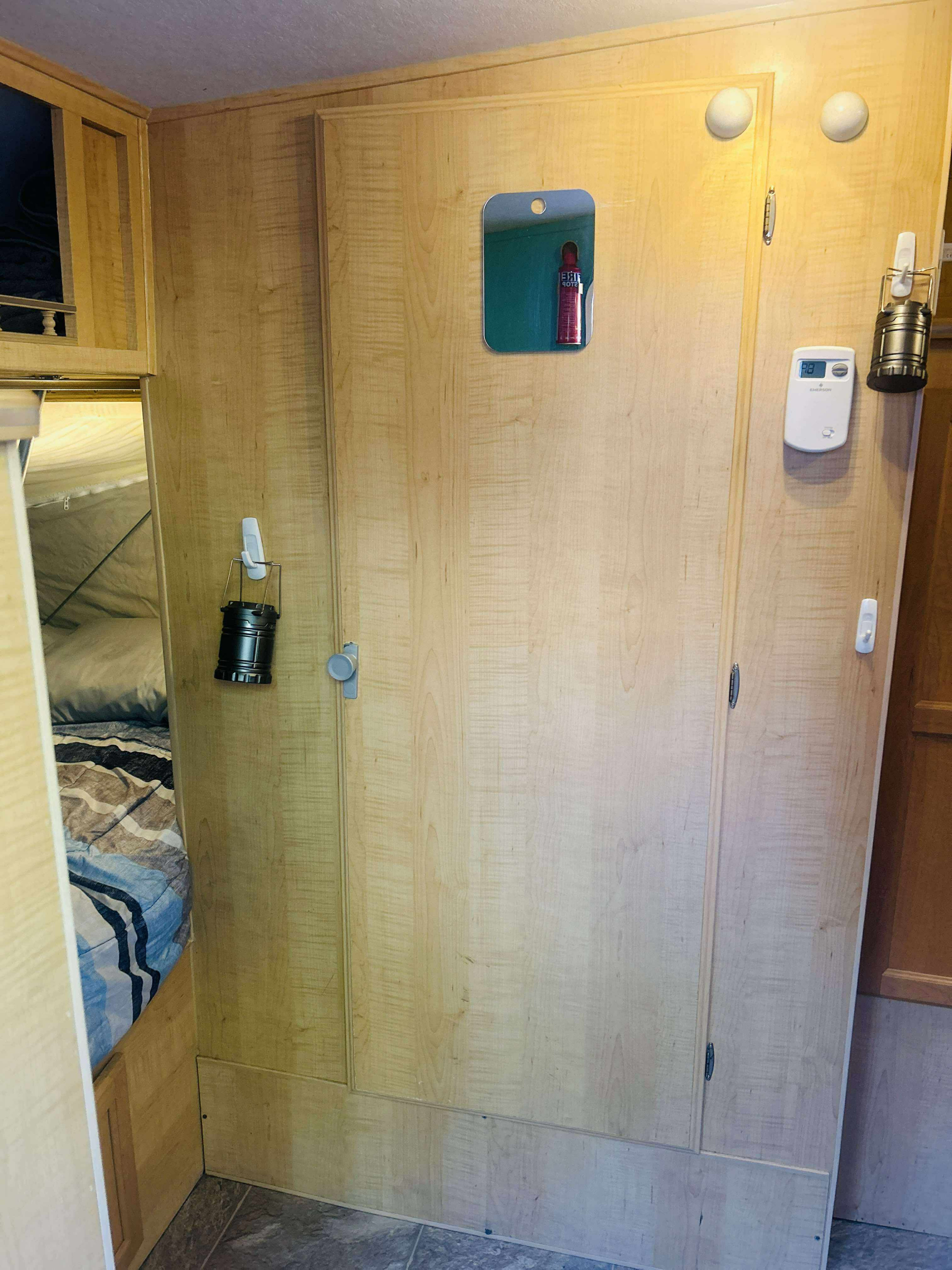 Inside an rv rental: light wood cabinetry with a mirror, thermostat, and hanging lantern. A comfy bed is glimpsed within.. Forest River M-17 2005