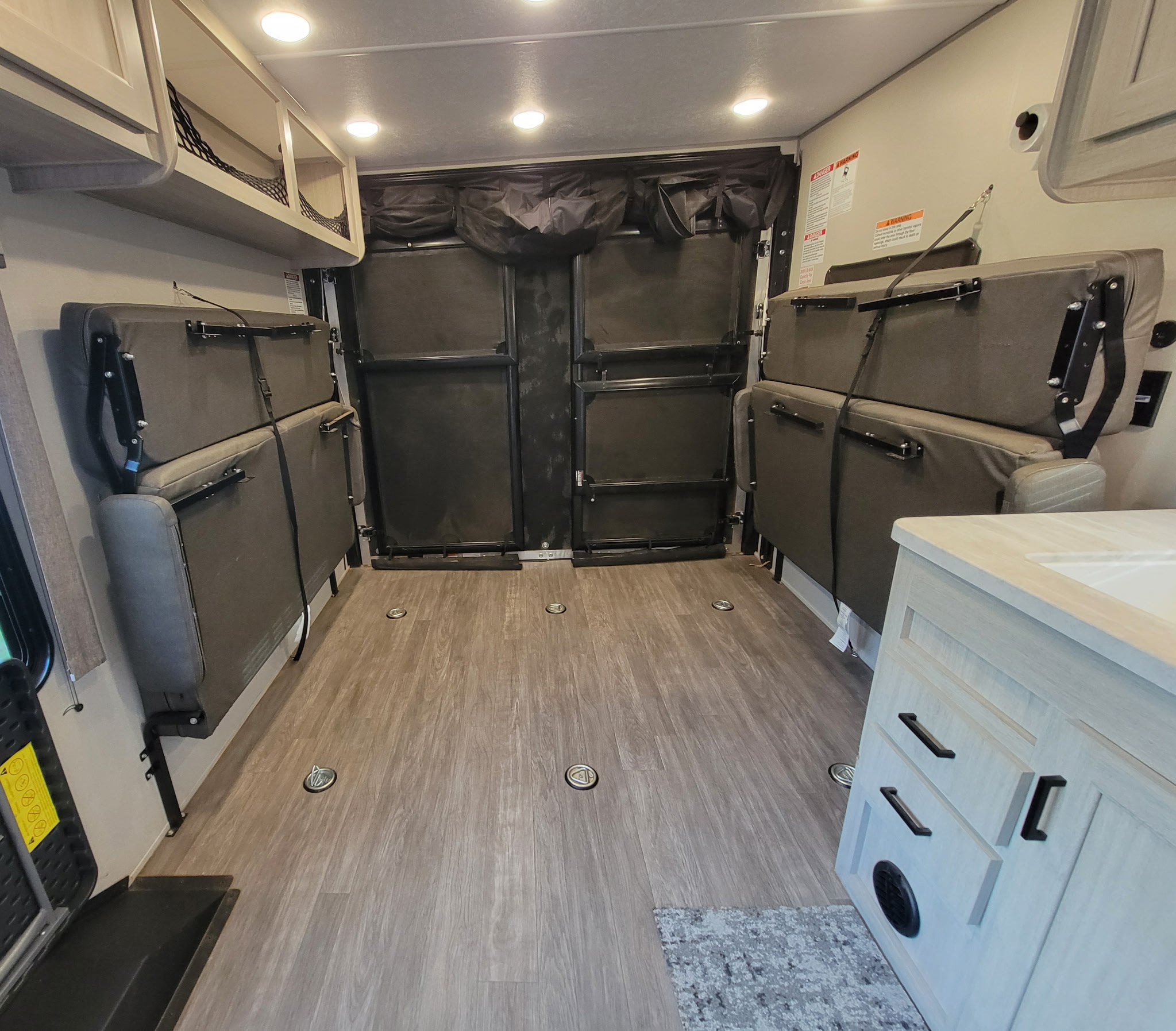 RV rental toy hauler interior: versatile cargo space with wall-mounted fold-up beds and floor tie-downs for secure travel.. Forest River Aurora Aurora Toy Hauler 2025