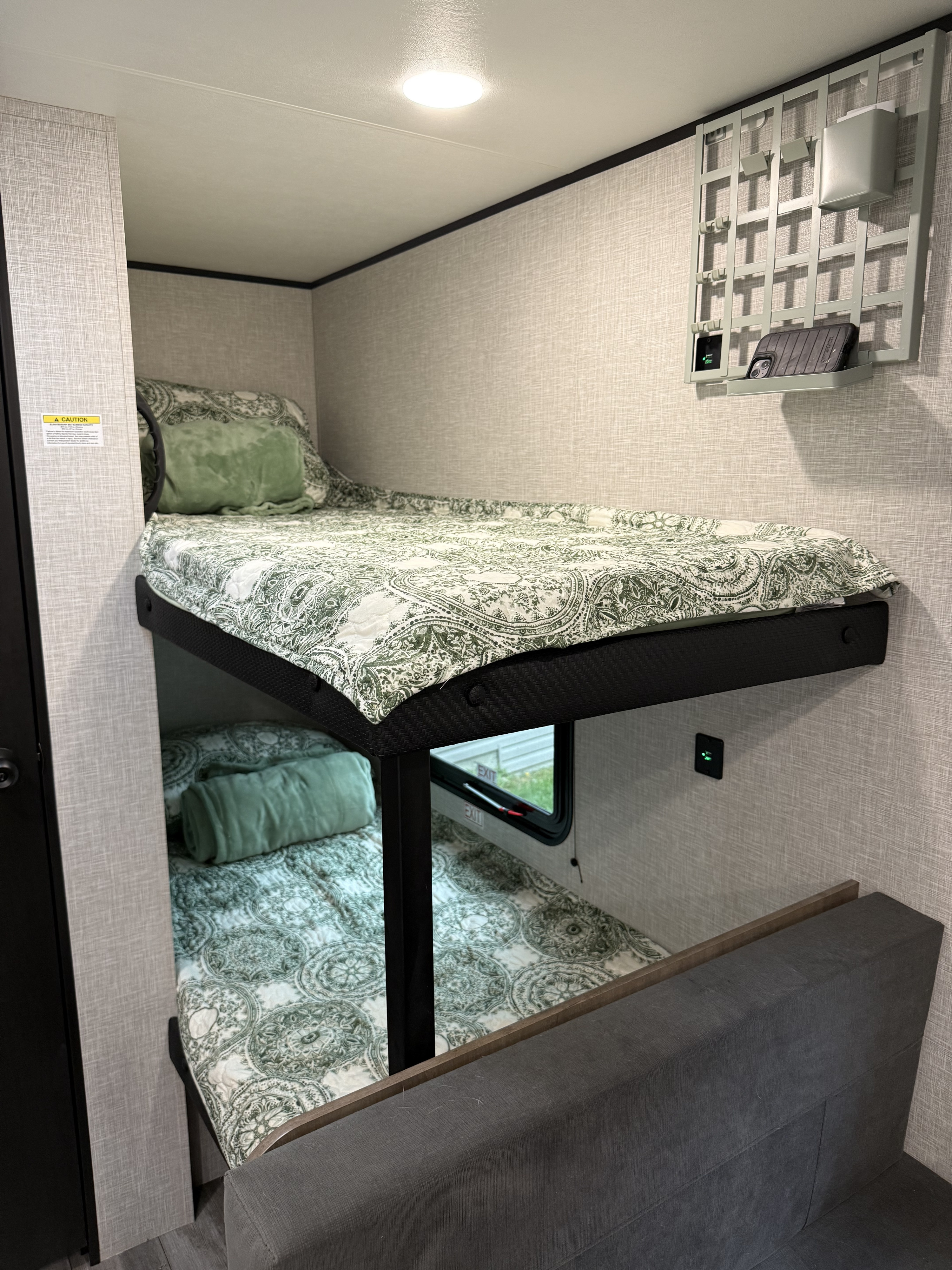 This RV rental features stacked bunk beds with green and white bedding, a wall-mounted organizer, and charging ports for a cozy sleeping area.. Jayco SLX Sport 2025