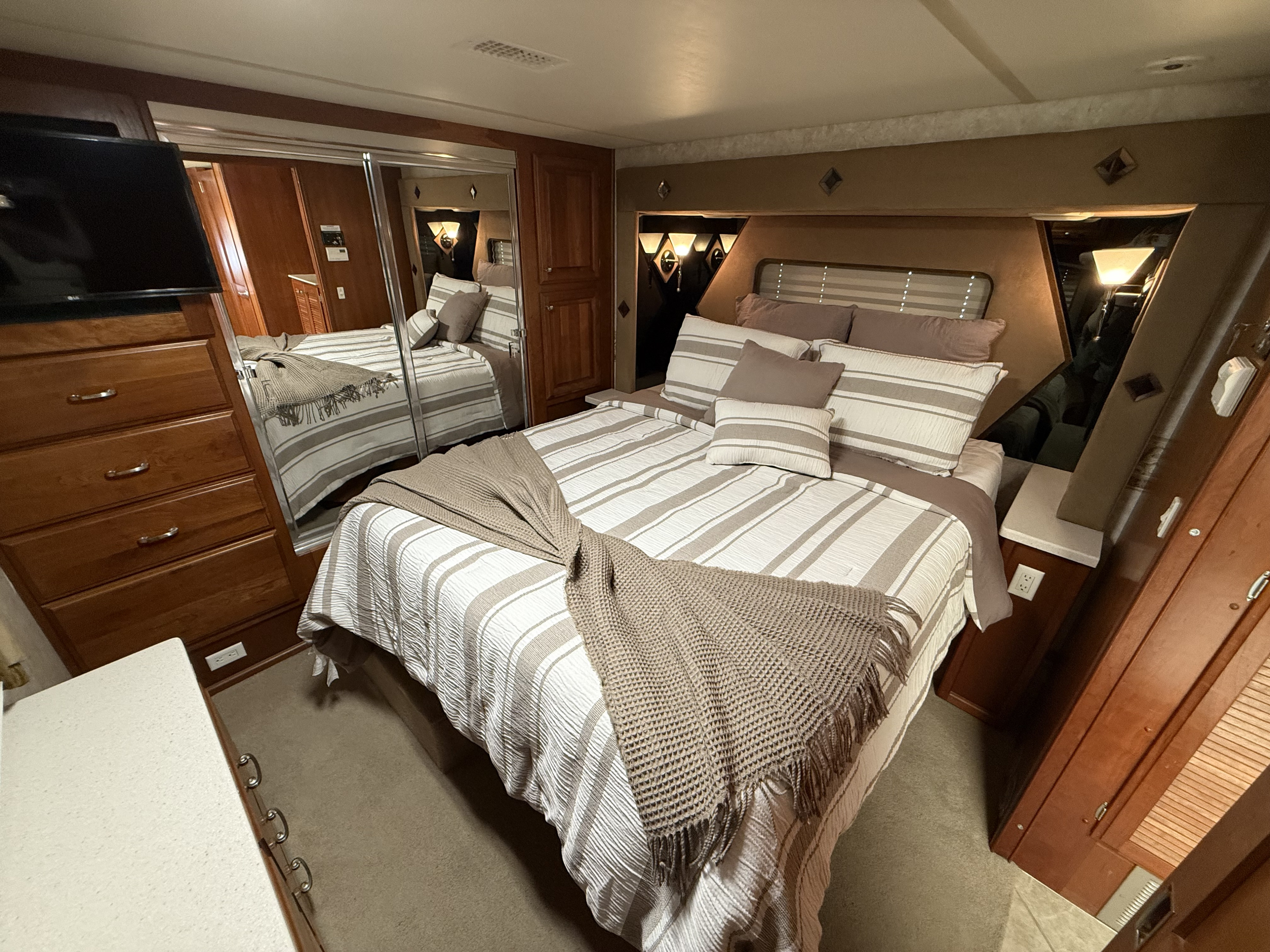 Modern RV rental bedroom with striped bedding, mirrored closet, and TV.. Fleetwood Revolution 2003