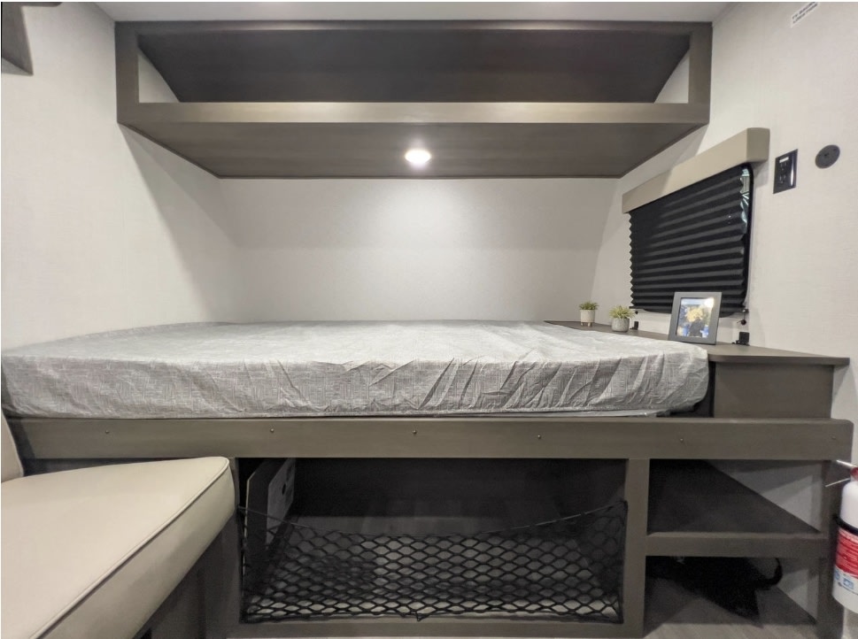RV rental's cozy sleeping area: a lower bed, overhead bunk, and under-bed storage with a net and shelving.. Grand Design Transcend One 151BH 2025