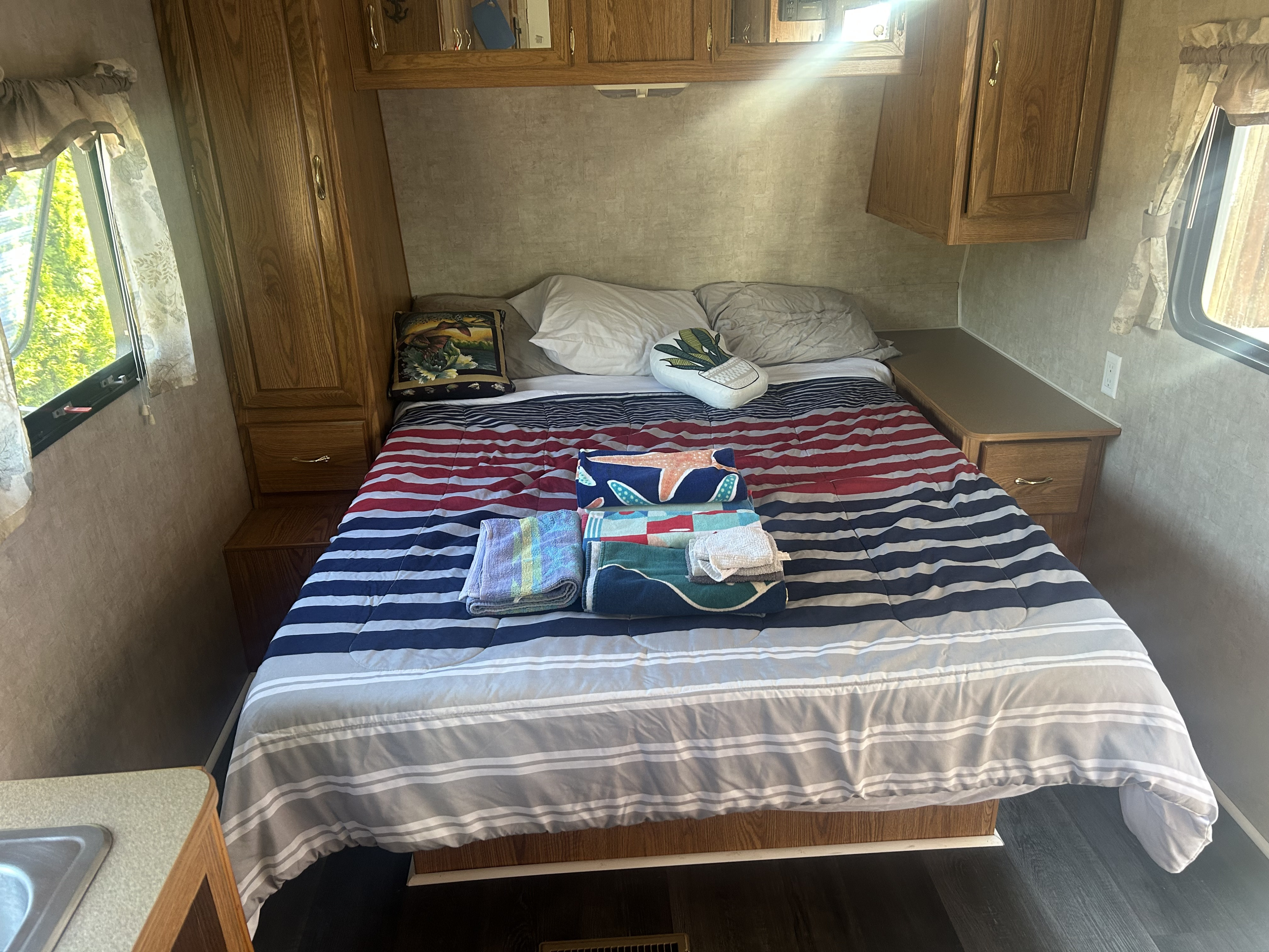 This RV rental offers a compact bedroom featuring a bed with striped bedding, built-in wooden cabinets, and bright windows.. Pioneer Pioneer Trailer 2006