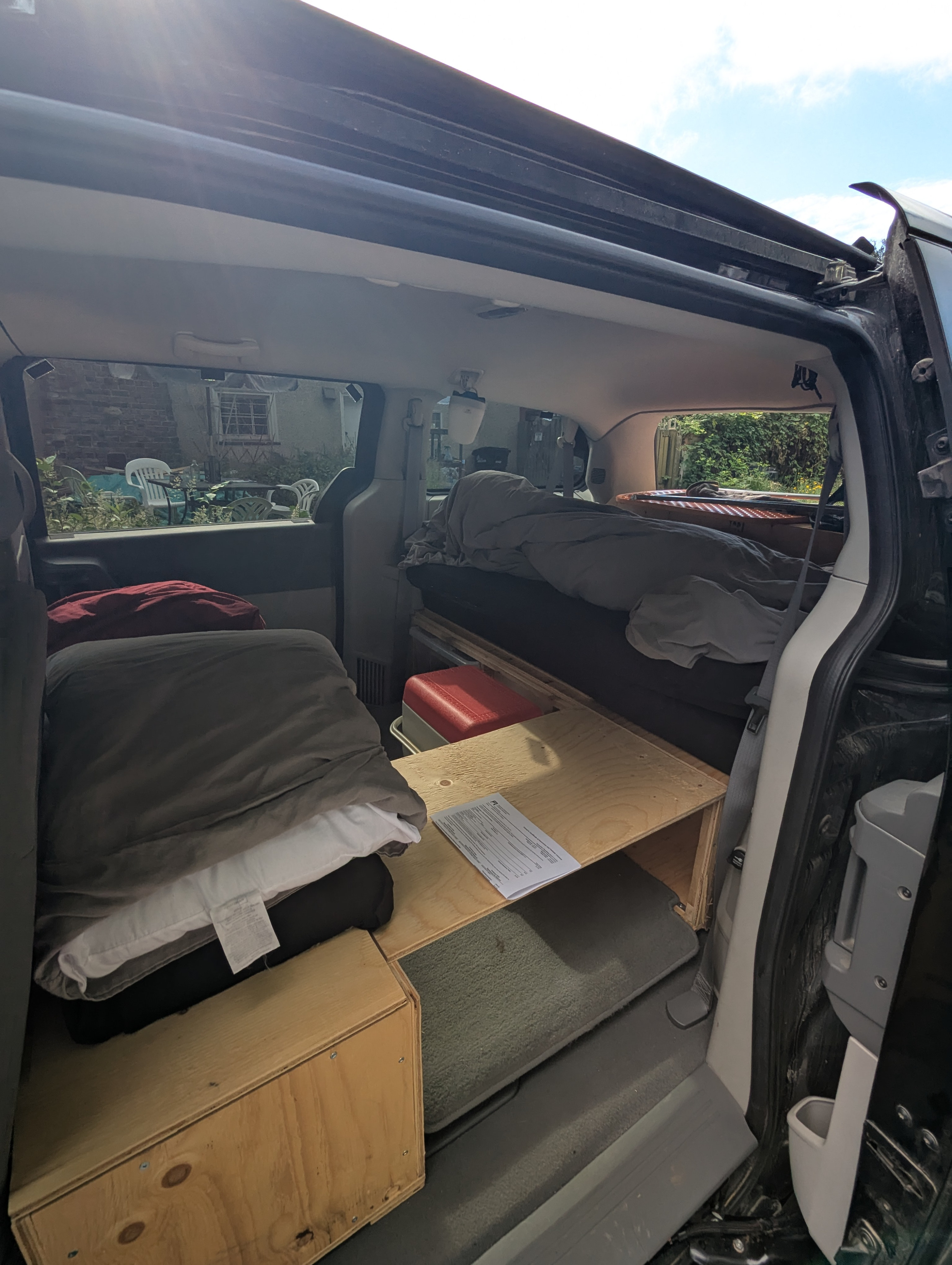 View inside an RV rental alternative: a minivan camper with sleeping setup, wooden storage, and cooler.. Dodge Grand Caravan 2009