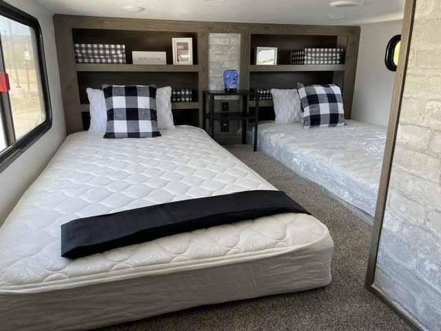 Discover a comfy RV rental bedroom featuring two twin beds (one still wrapped), built-in shelves, & cozy decor.. Forest River Sabre 2021