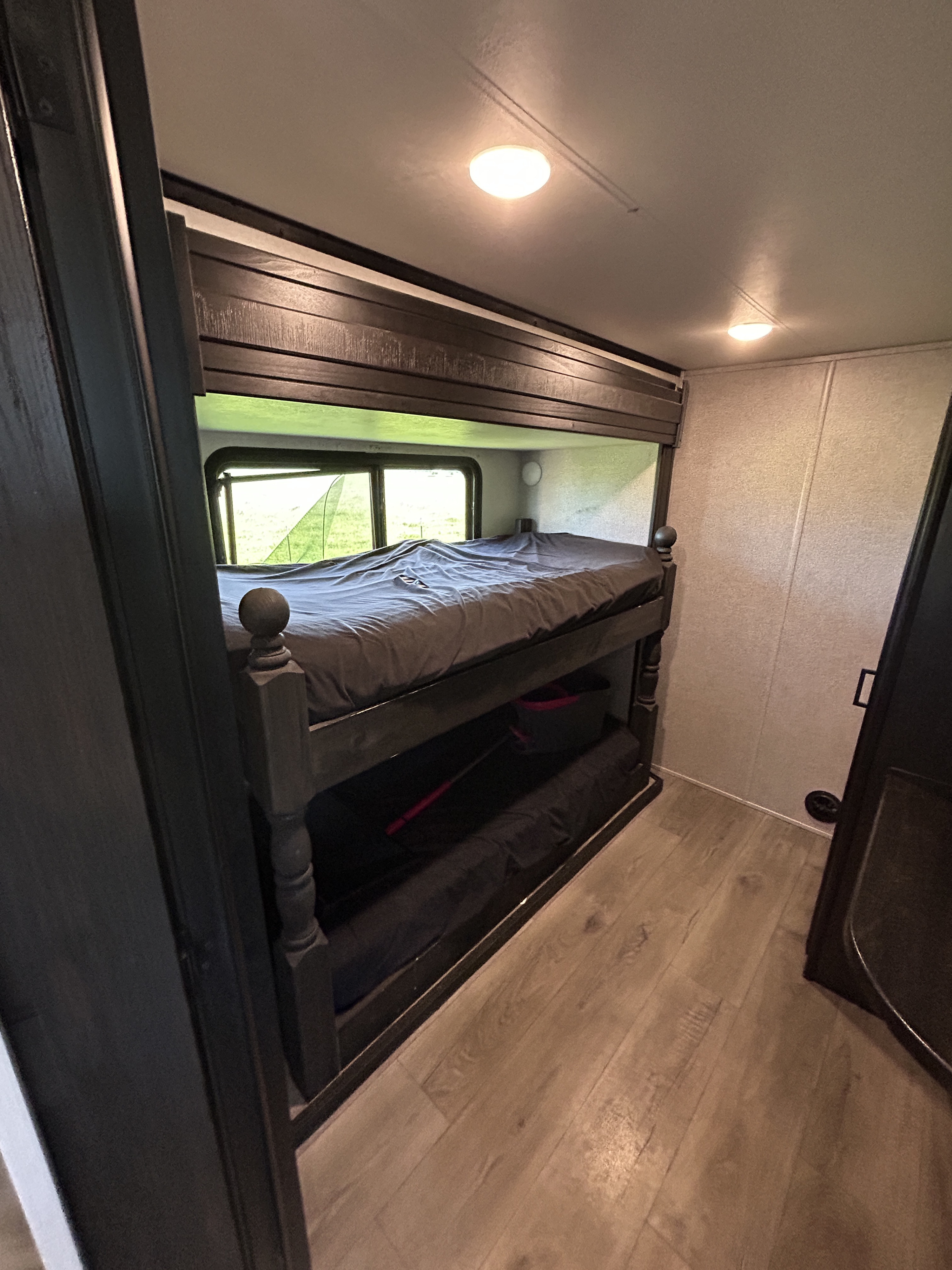 RV rental interior features cozy dark wood bunk beds with grey bedding, bright ceiling lights, and a scenic window.. Highland Ridge RV Open Range 2021