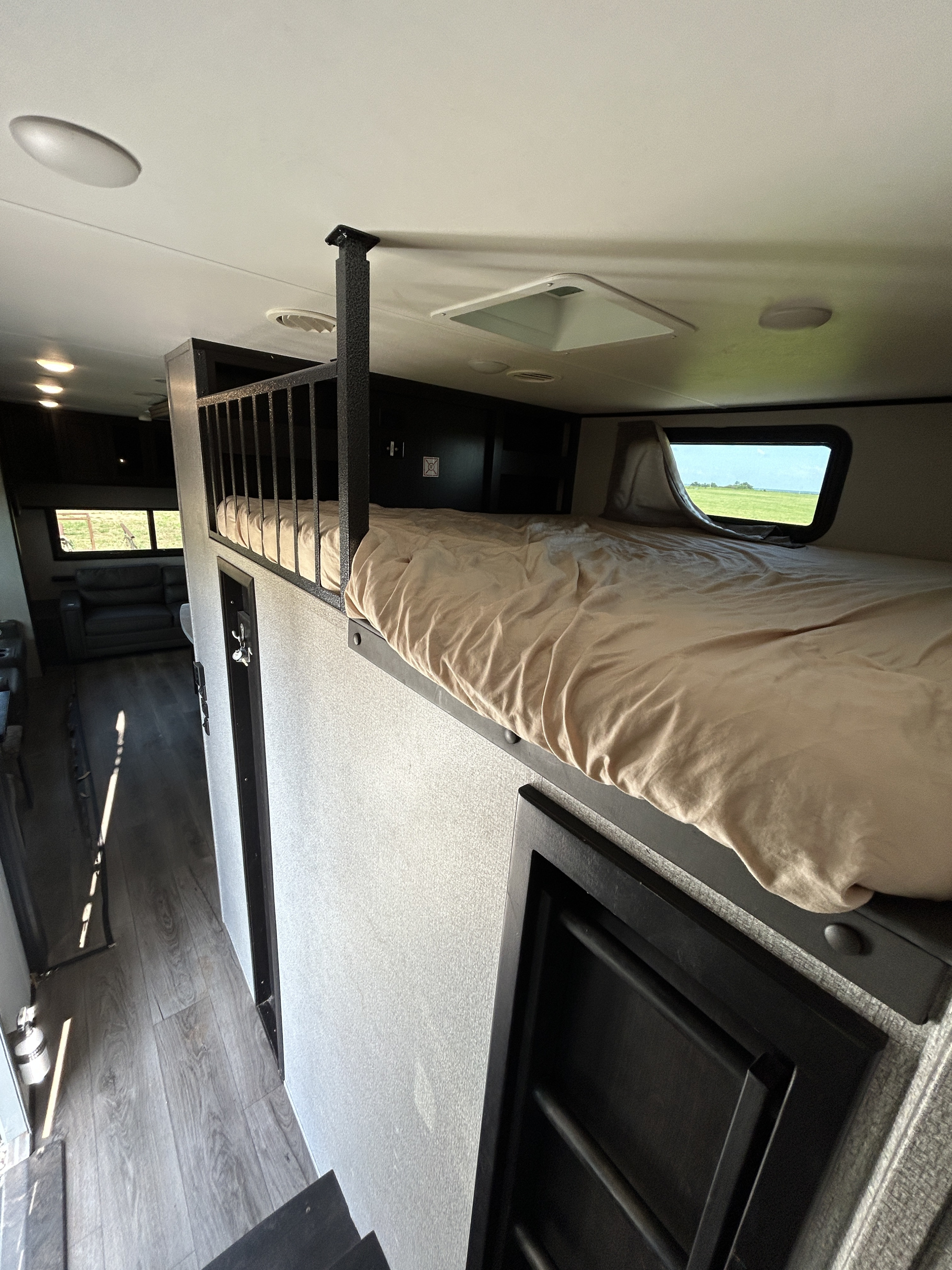Inside an RV rental: a comfortable bunk bed with a railing, a window overlooking a field, and a glimpse of the living area.. Highland Ridge RV Open Range 2021