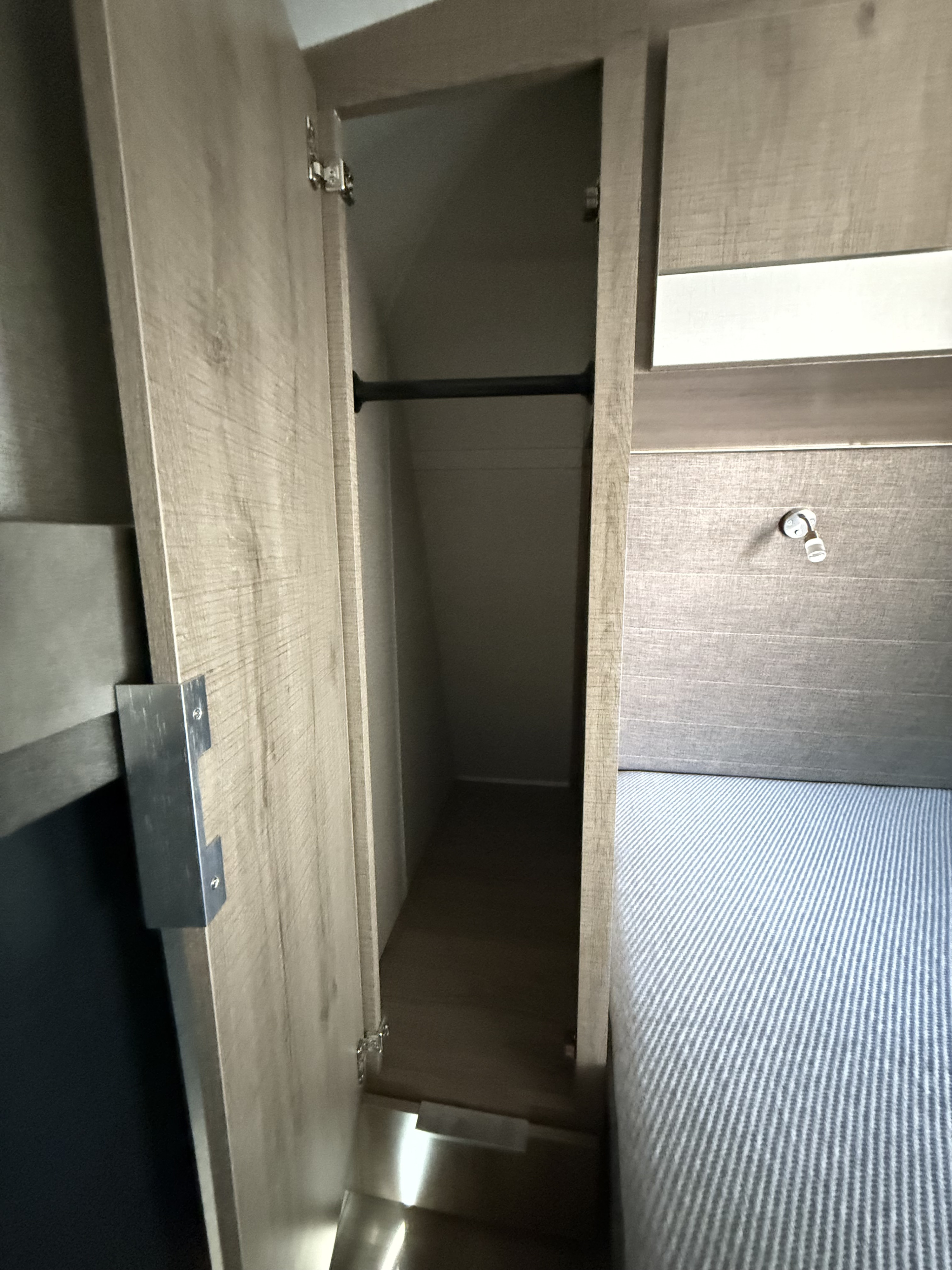 RV rental: Open wardrobe with hanging rod next to a bed with blue striped bedding.. Grand Design Imagine 2020