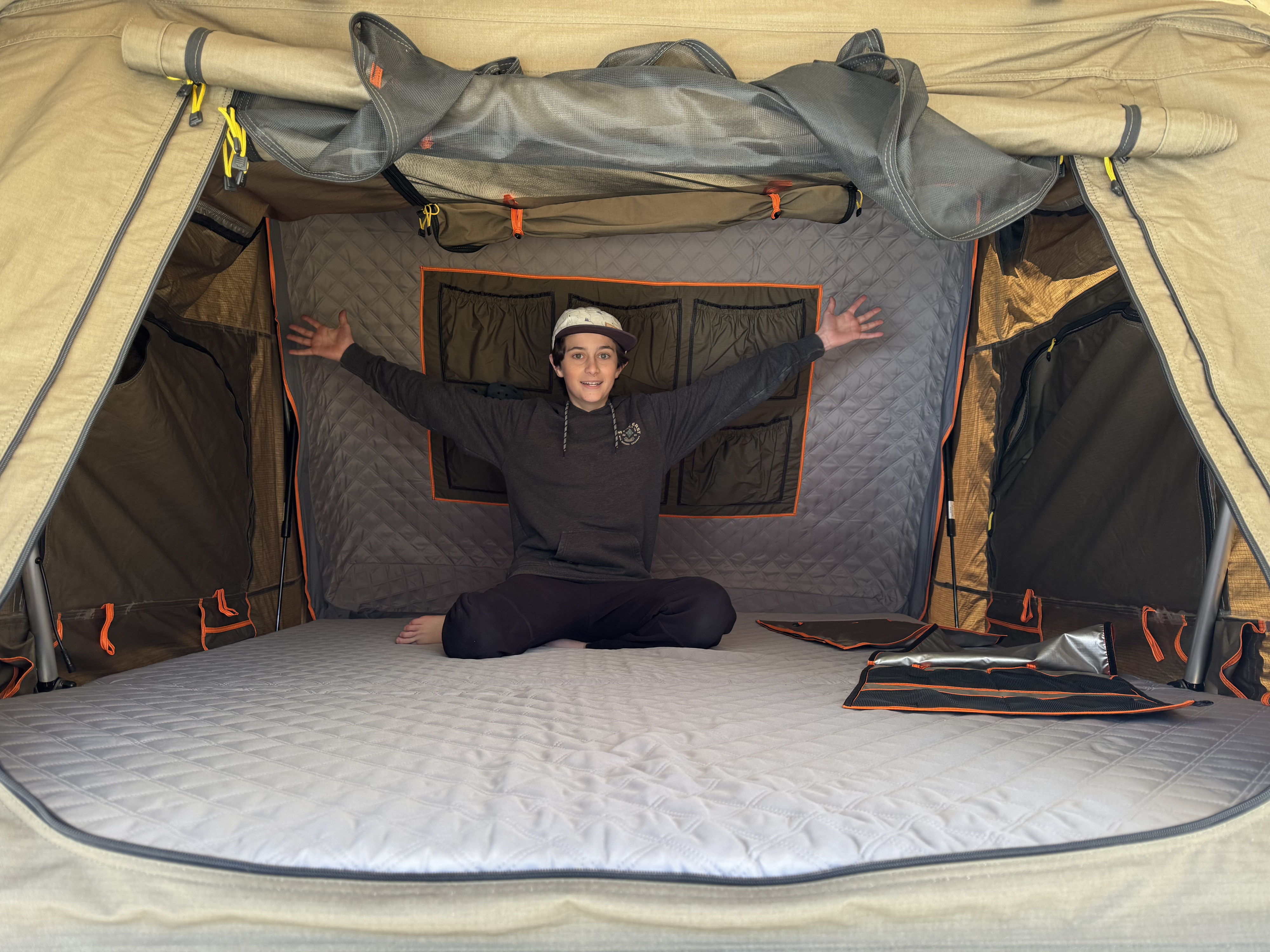 Happy youth in RV rental rooftop tent. See its comfy mattress, storage pockets & mesh windows, great for travel & camping!. Tribe Overland Basecamp/Expedition 2022