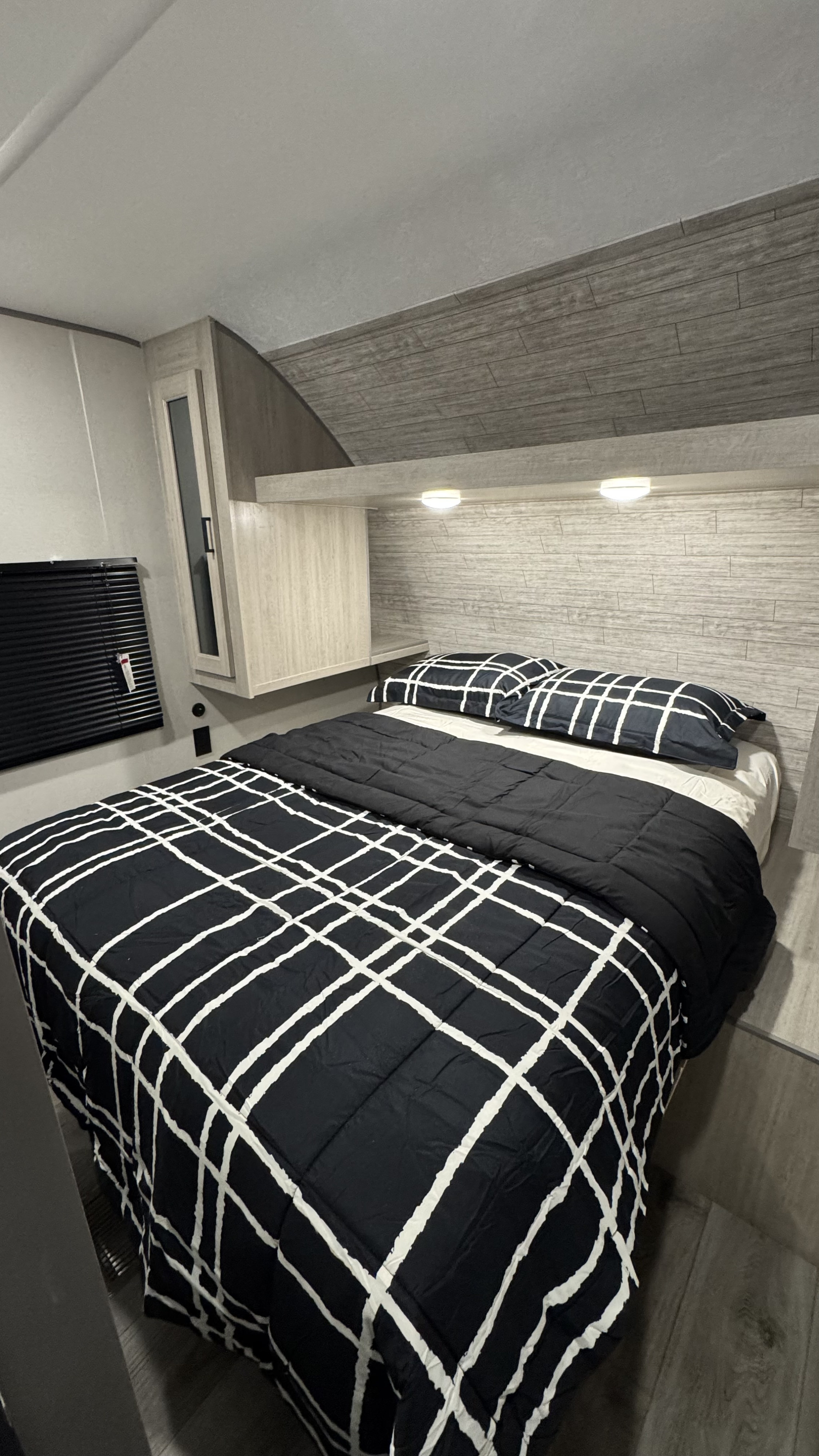 Comfortable RV rental bedroom featuring a modern bed with black and white bedding, built-in storage, and warm ambient lighting.. Coachmen Catalina 2025