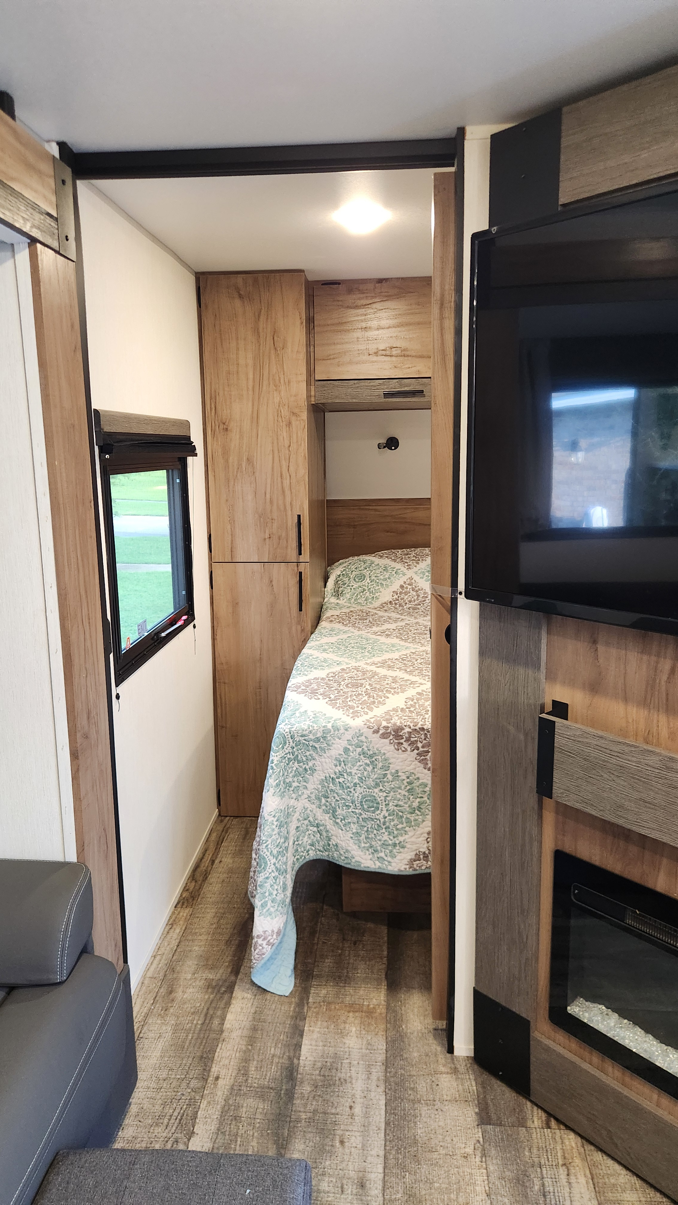 Modern RV rental interior showing a compact bedroom with a bed and cabinetry, plus a living area with TV and fireplace.. Forest River Campsite Reserve 26cj 2025