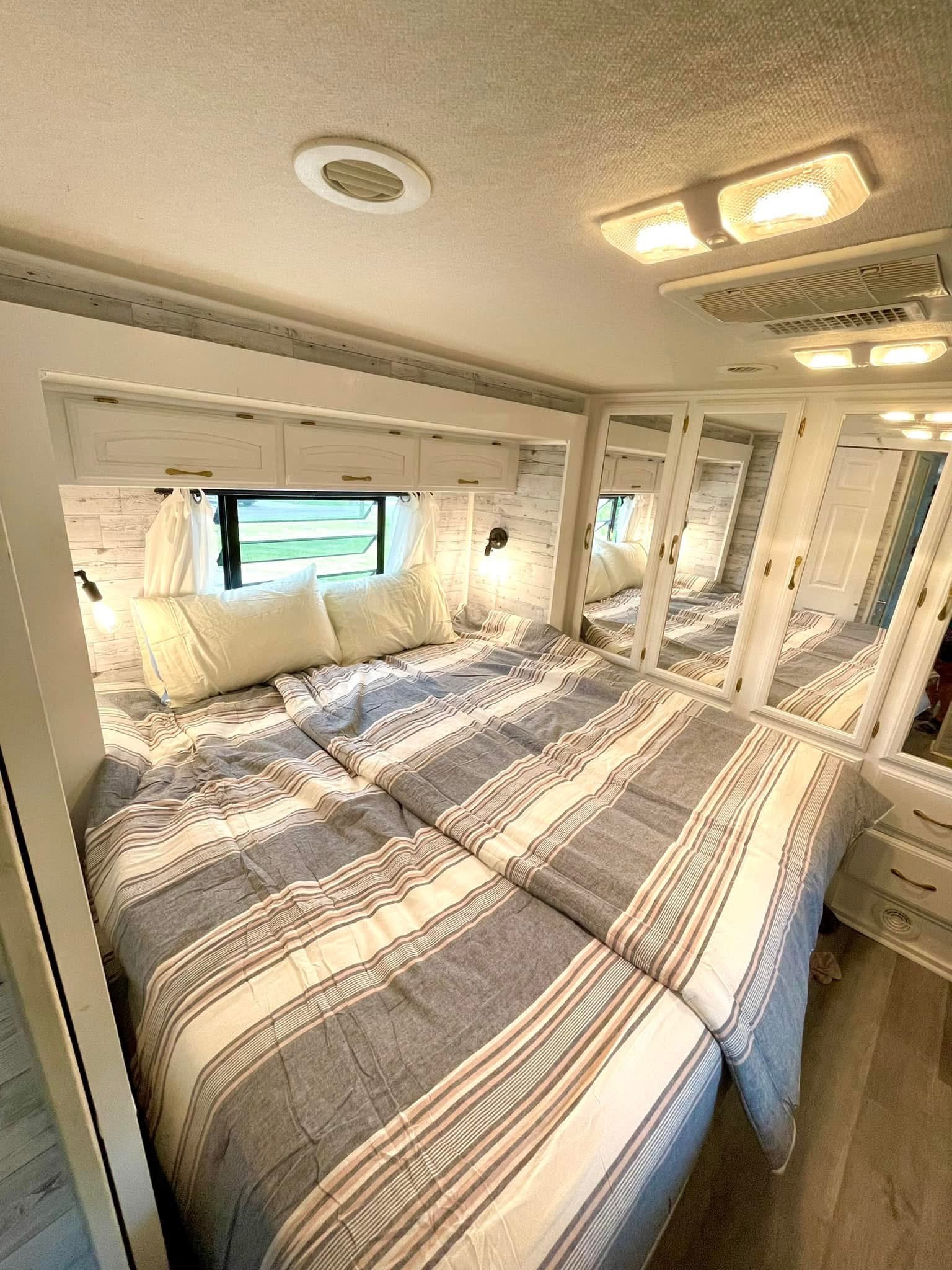 Modern RV rental bedroom with striped bed, white cabinets, mirrored wardrobe, AC, and lighting.. Georgie Boy Landau 2004