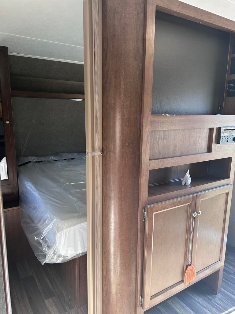Explore a clean RV rental interior: view of a protected mattress in the bedroom nook and built-in wood cabinetry with storage.. Keystone RV Hideout 2017