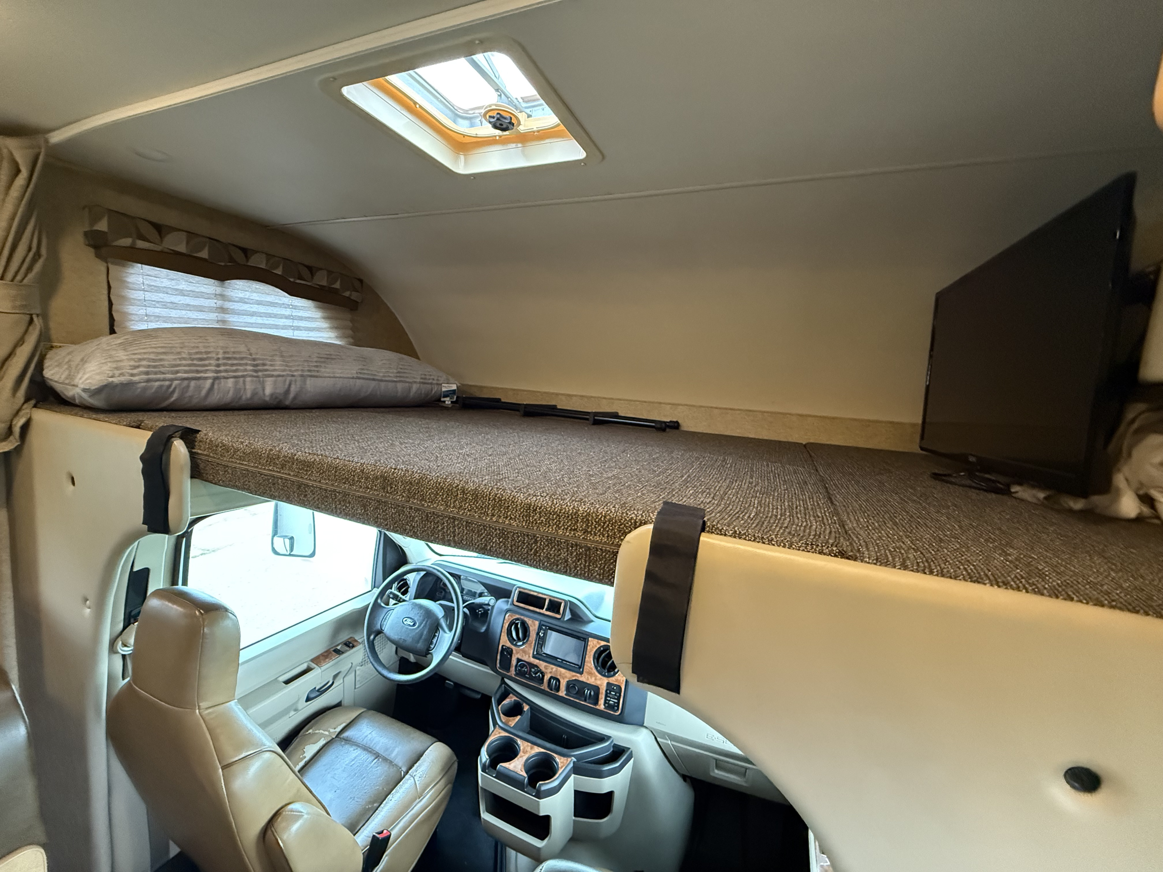 Interior of an RV rental, featuring the front cab-over sleeping bunk with a TV, overlooking the driver's area.. Thor Chateau 2017